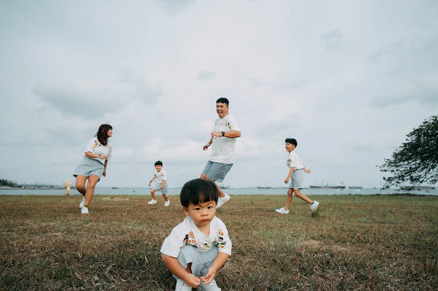 Family with three young children running and playing on the grass at Marina Barrage