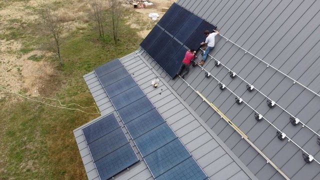Two workers installing or maintaining solar panels on a sloped metal roof.