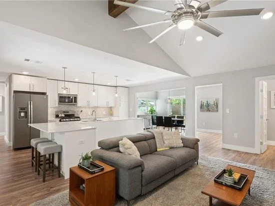 Open-concept living room and kitchen with gray sofas, a kitchen island, and dining area in a modern home.