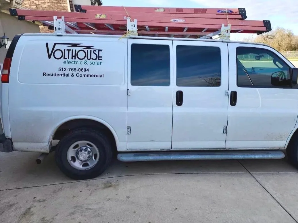 White commercial van with business logo 'Volthouse electric & solar' on the side, parked on a concrete driveway, carrying a ladder on top.