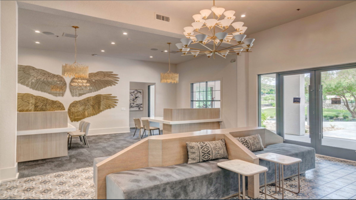 Modern lobby with cream-colored walls, a large light fixture, decorative wall art of gold wings, comfortable seating, and large windows