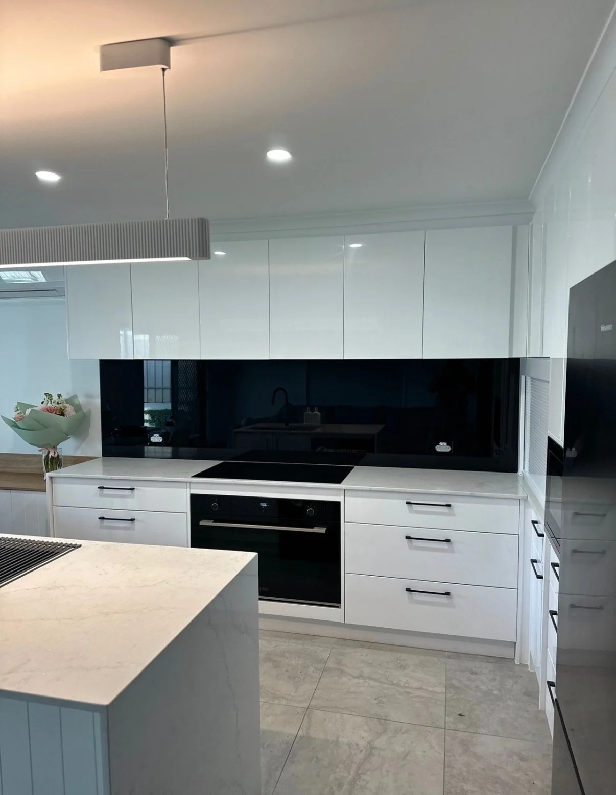 Modern kitchen with white cabinets, black cooktop, built-in oven, marble countertop, and a bouquet of flowers on the side