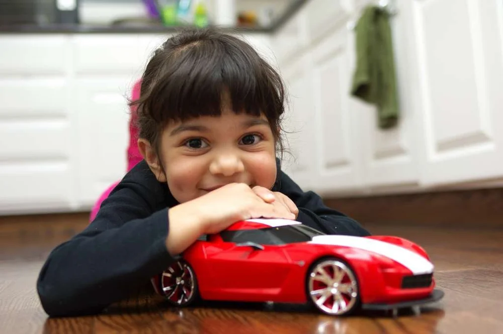 Ana Palestro as a small child, lying on the floor and hugging a red toy race car with white stripes