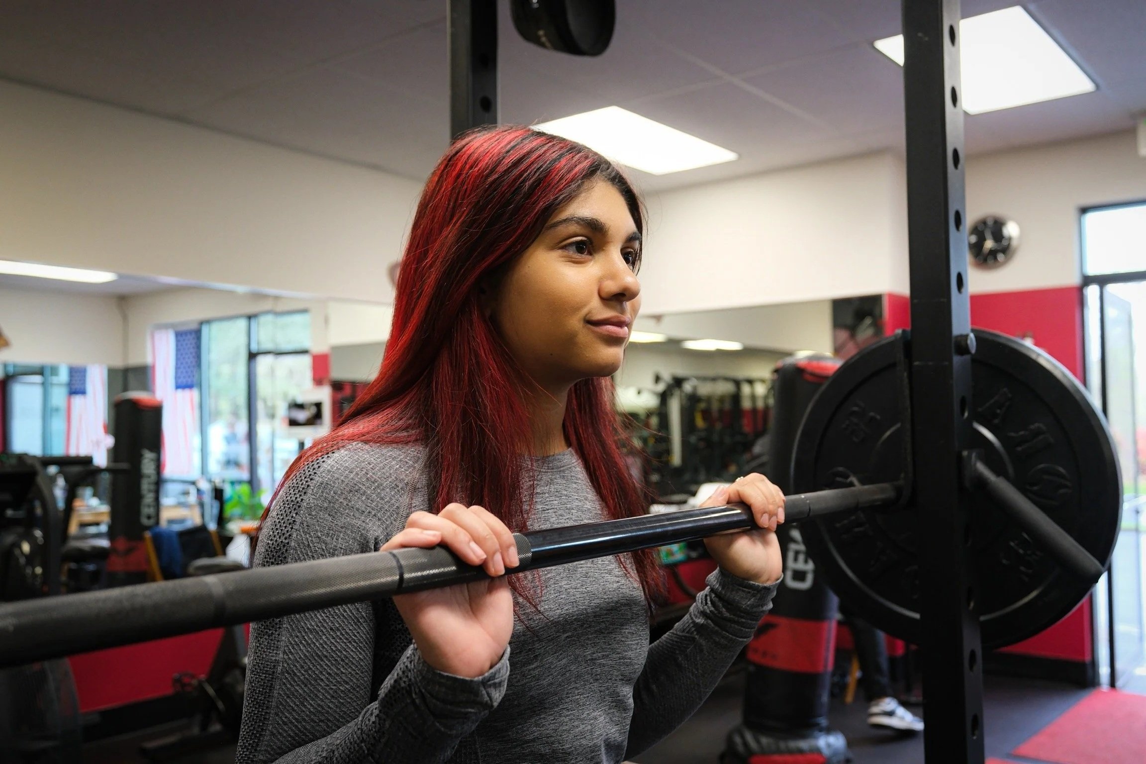 A young woman with red hair practicing squats with a barbell at a gym.