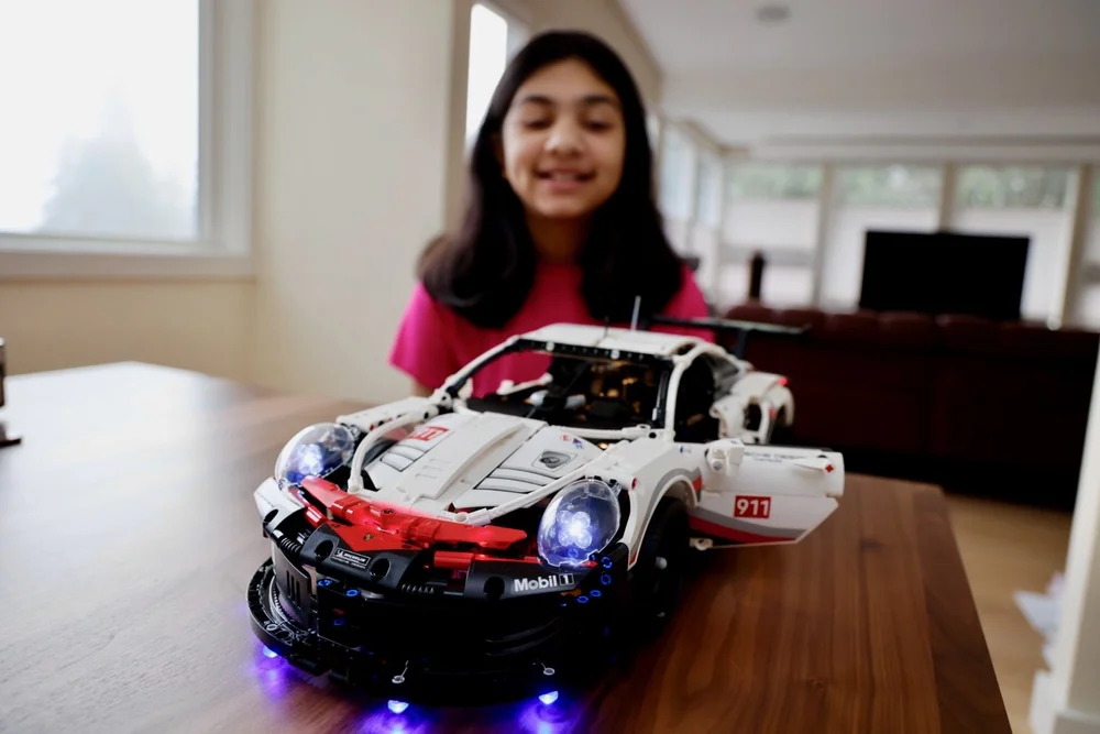 Ana Palestro at age 12 in January 2022, smiling behind her lit-up LEGO Technic Porsche 911 RSR on a wooden table
