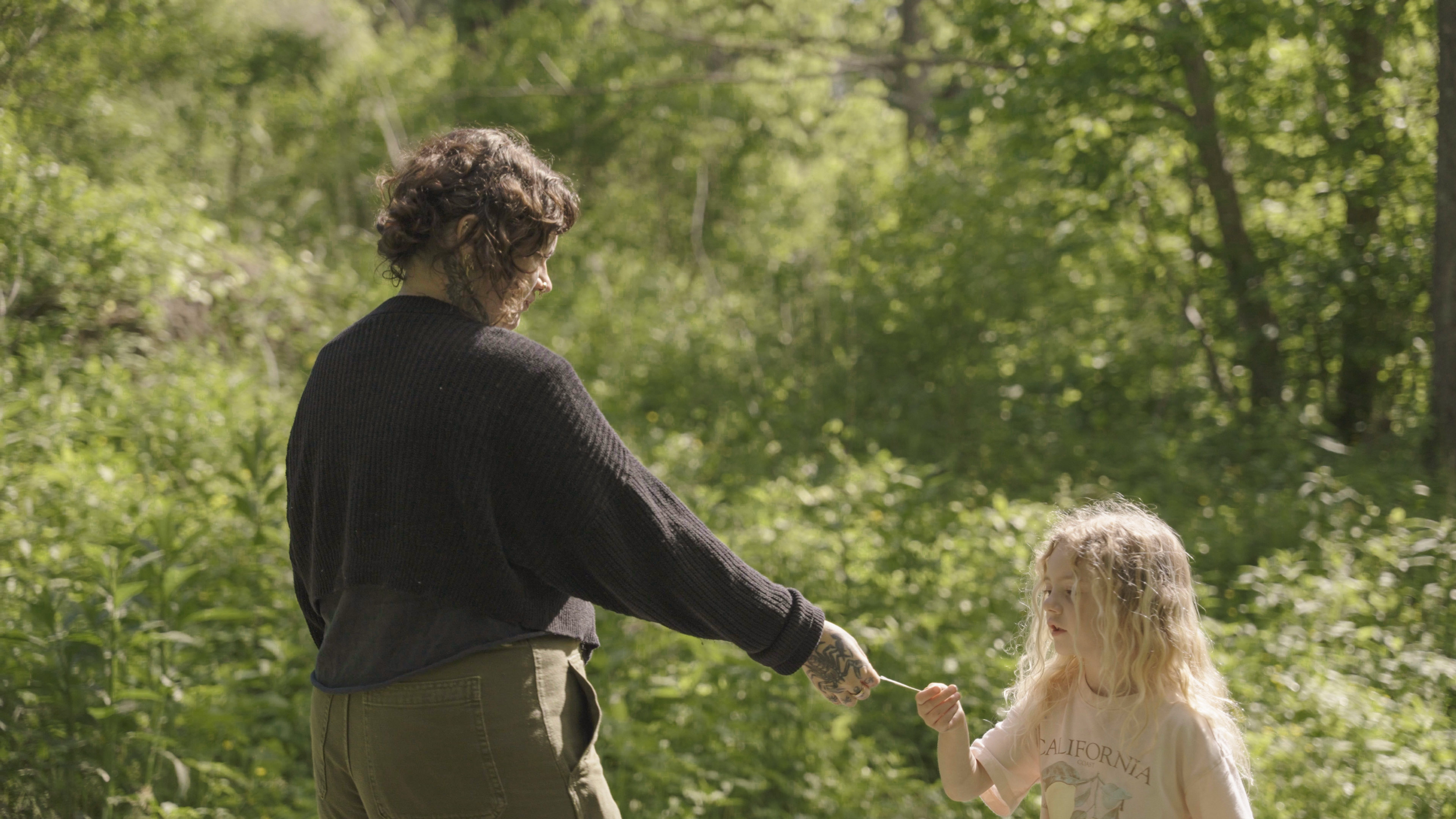 A woman is handing a flower to a young girl in a lush green forest.