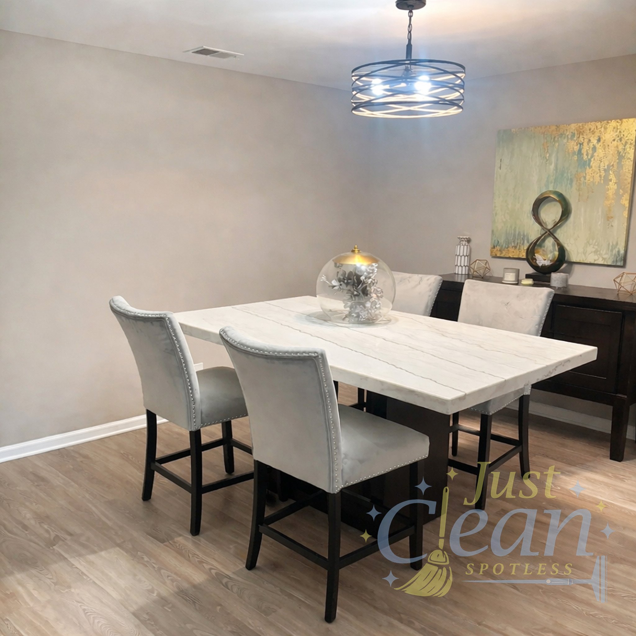 A modern dining room with a white marble table, four upholstered chairs, a black sideboard, a decorative sculpture, and a gold-framed mirror. A contemporary chandelier hangs above the table, and there's a large abstract painting on the wall.