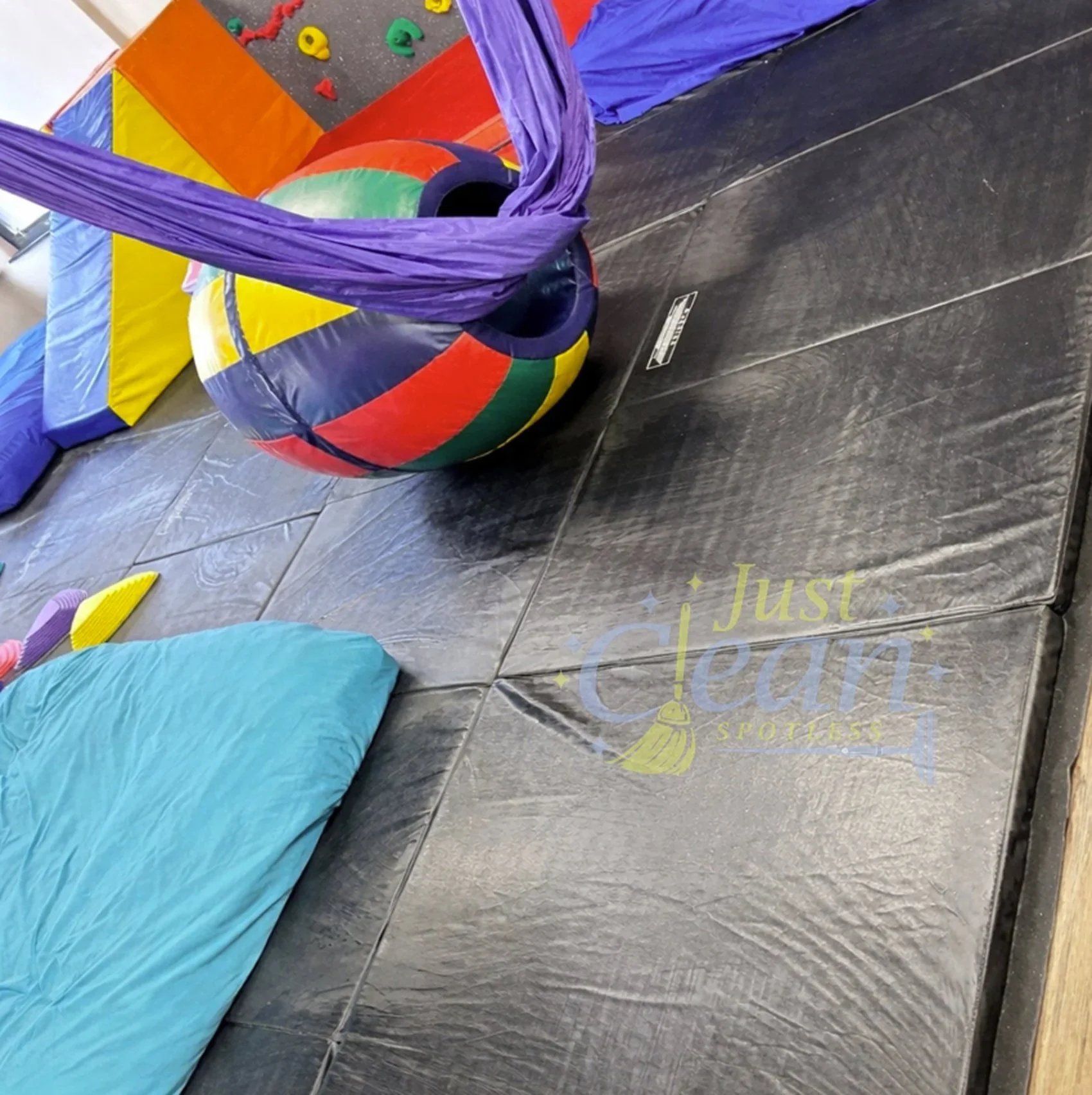 Colorful indoor climbing gym with padded floor, climbing holds, and aerial silks.