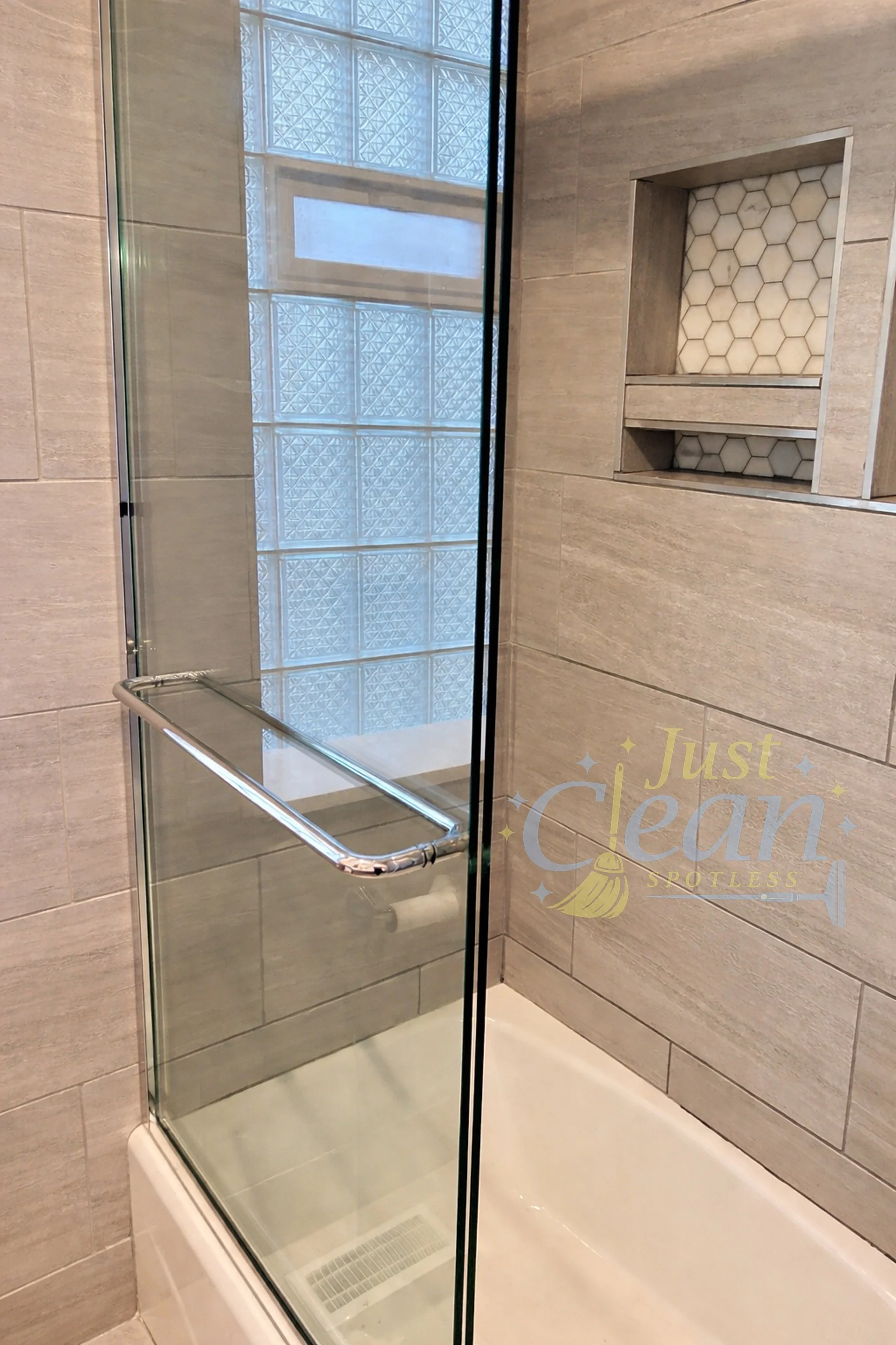 A glass shower door with a metal handle in a modern bathroom with beige tiled walls and a built-in niche.