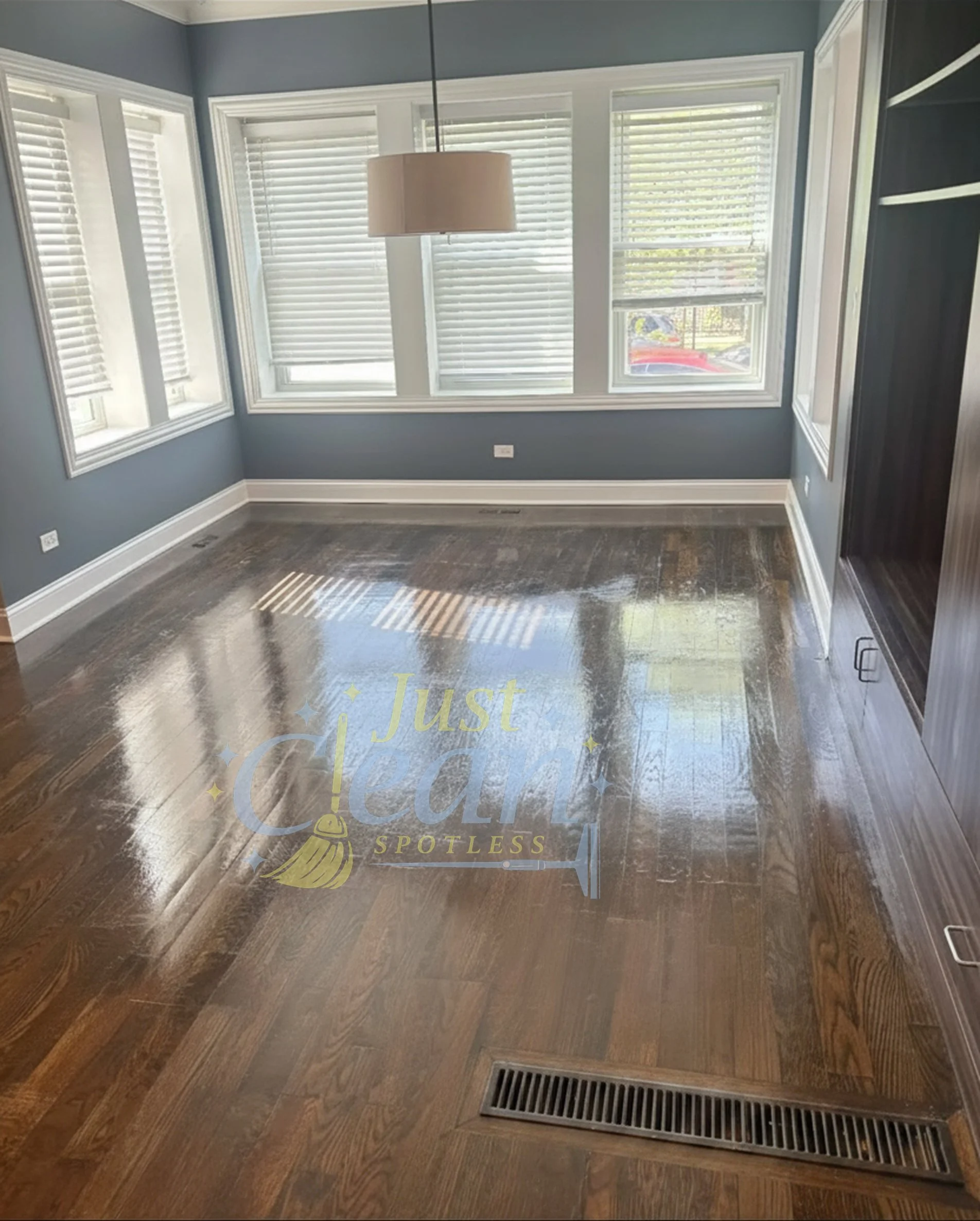 A room with large windows covered with white blinds, blue walls, and a hardwood floor. There is a heat vent on the floor near the bottom of the image.