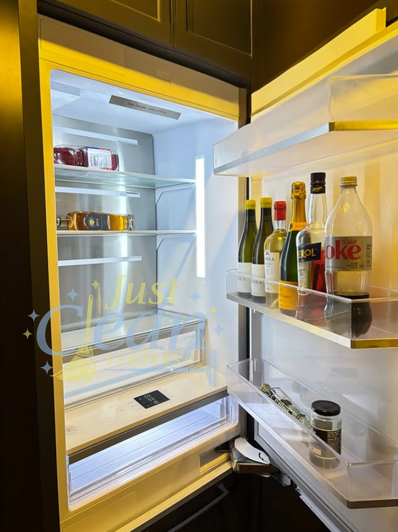 Open refrigerator with empty shelves and a few bottles of beverages, including wine and soda, on the door. The interior light is on, revealing a modern design with clear storage compartments.