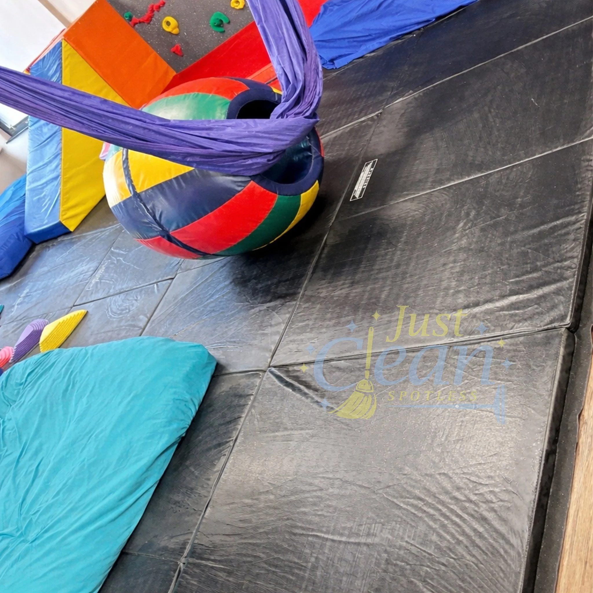 Colorful indoor playground equipment including a rainbow ball, climbing structures, and foam mats.