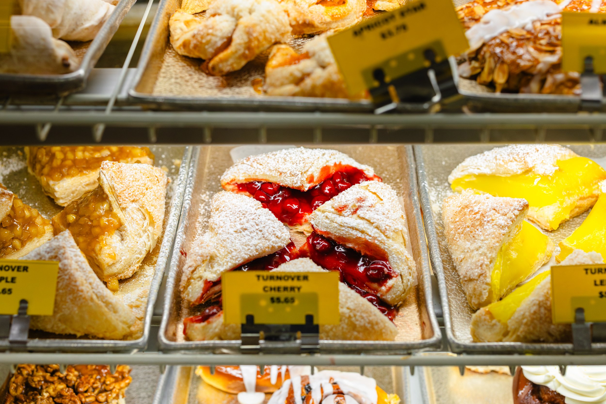 Display of assorted slices of dessert pies in a bakery showcase, including cherry pie with filling spilling out, lemon pie, and other fruit-filled pies.