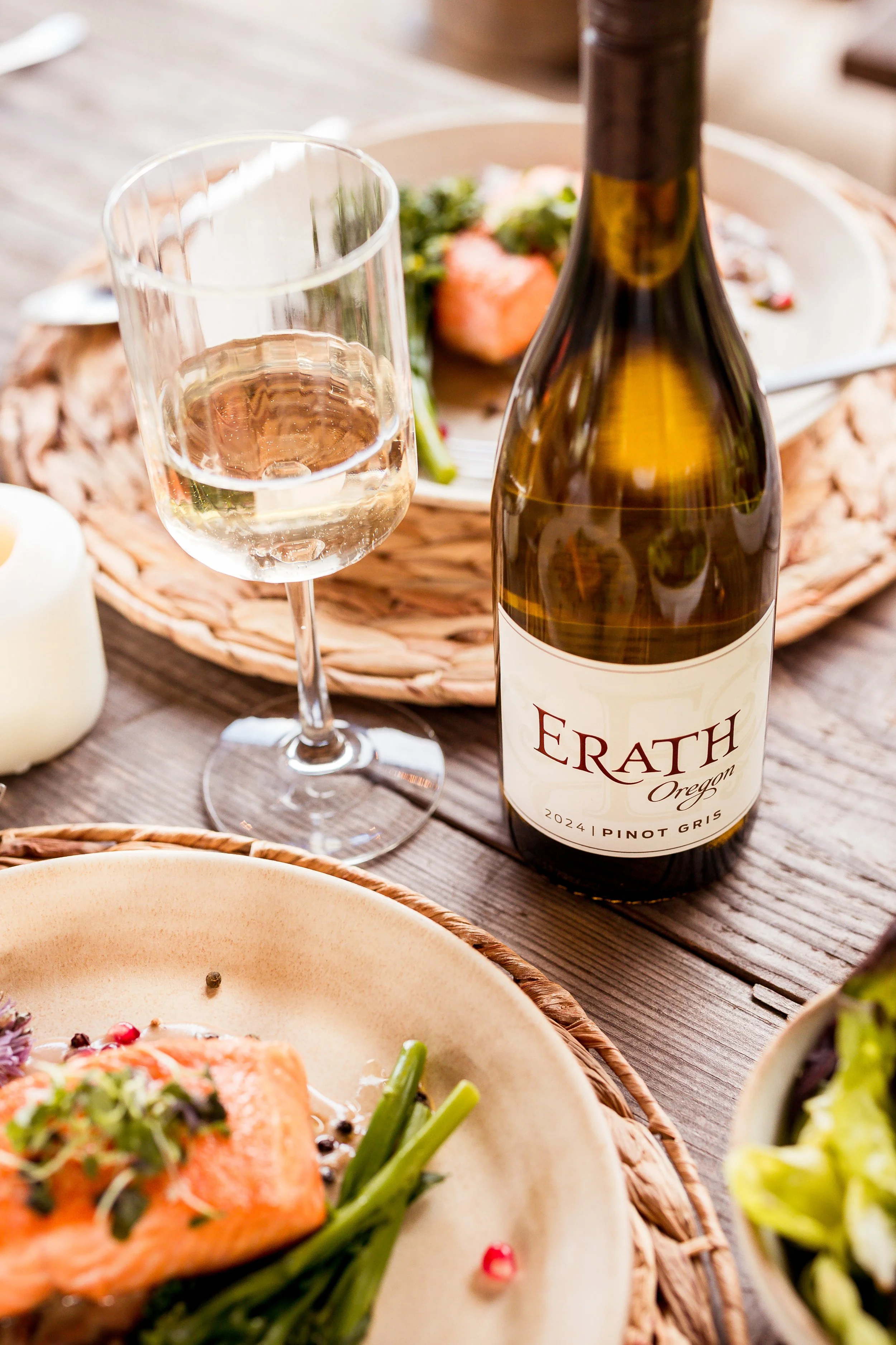 A table with a glass of white wine, a bottle of Erath Pinot Gris, a bowl of salmon, green beans, salad, and a white candle.