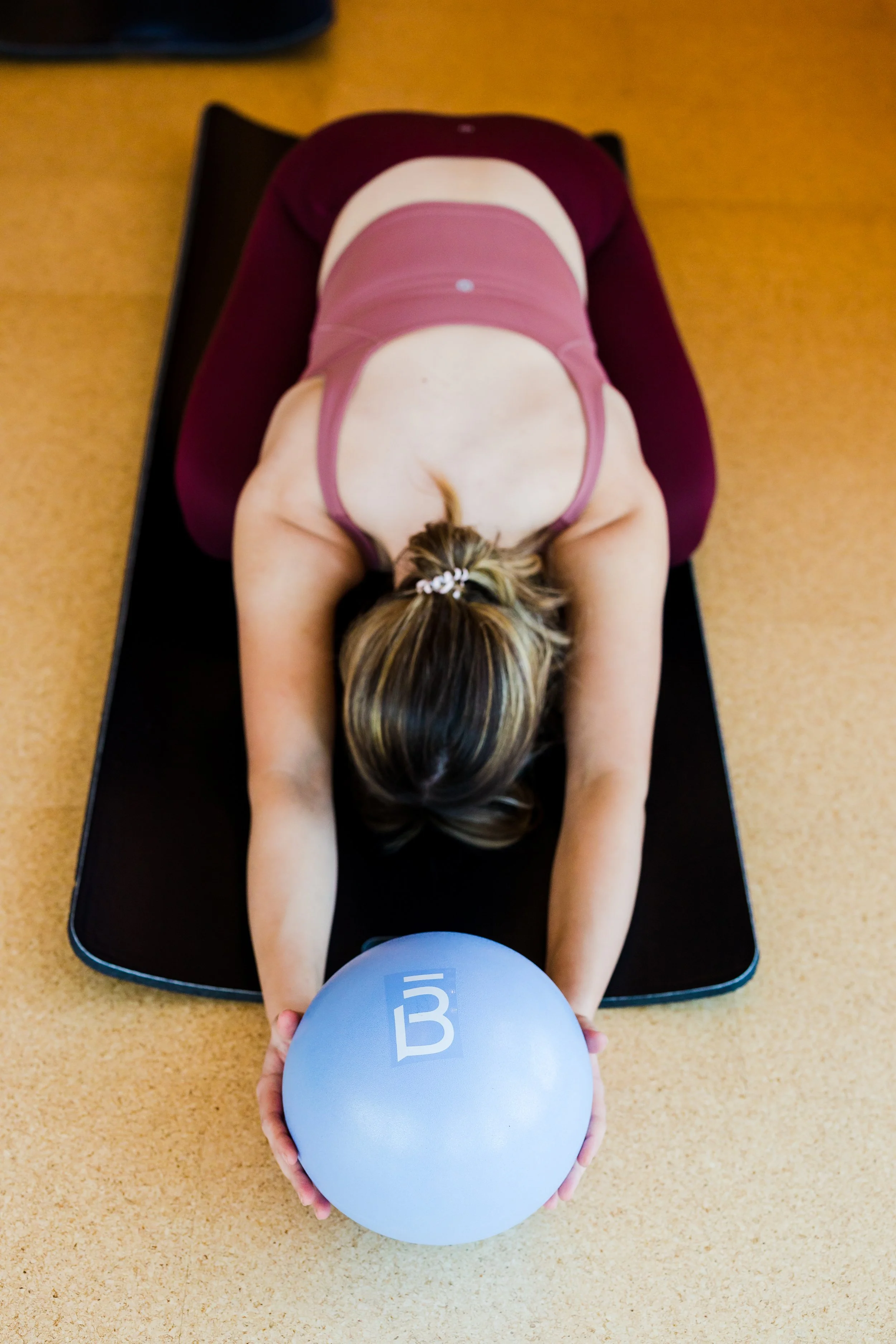 Woman in yoga pose on yoga mat, holding exercise ball in gym or fitness studio.
