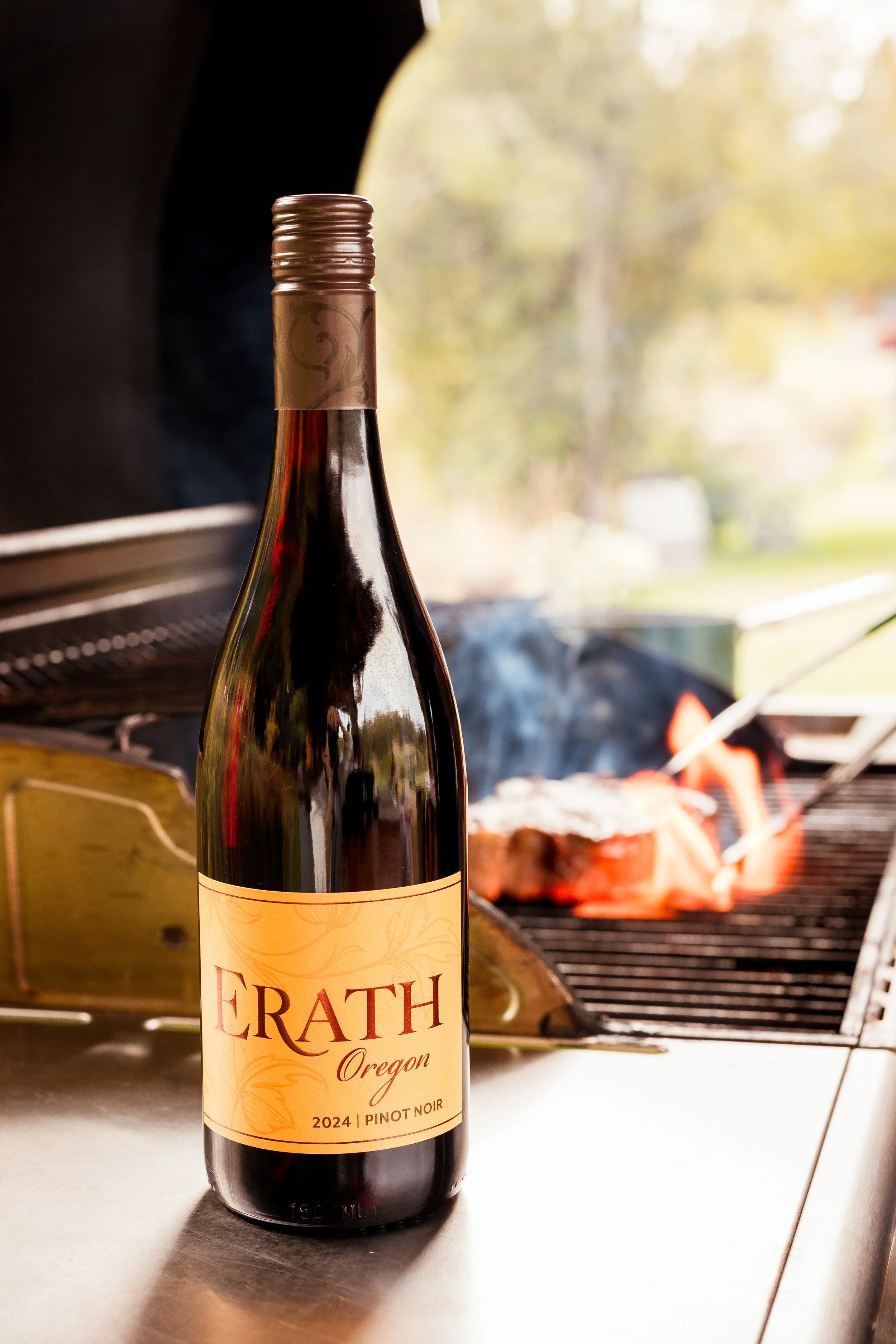 A bottle of Erath Oregon Pinot Noir wine on a kitchen countertop with a grill in the background where meat is being cooked.