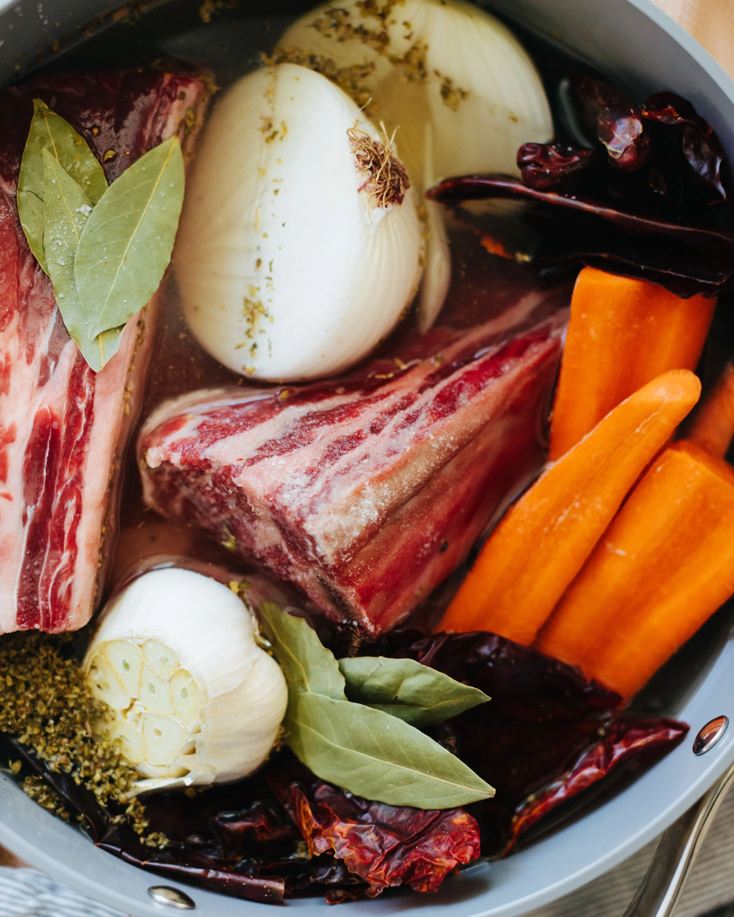 Raw beef, garlic, carrots, dried chili peppers, bay leaves, and spices in a pot for cooking.