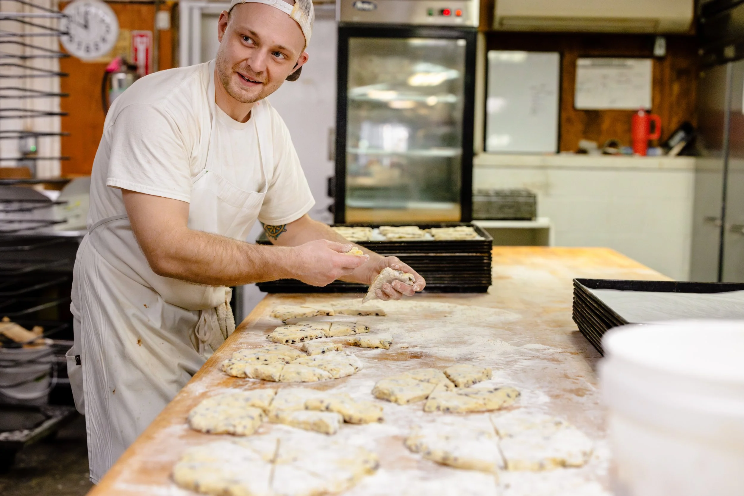 A man in a white t-shirt and apron making cookies in a bakery kitchen.