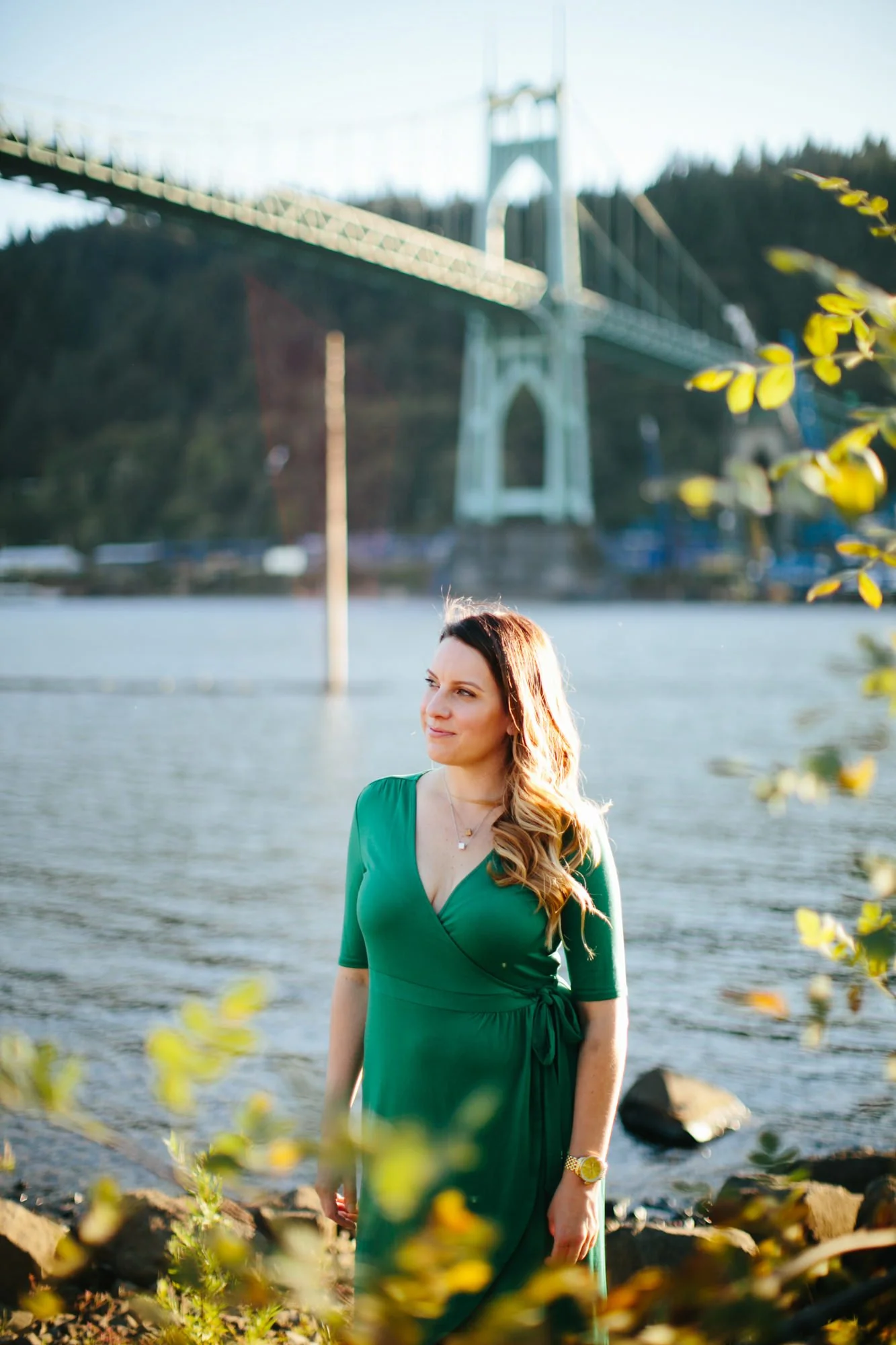 A woman in a green dress standing by the water with a bridge in the background