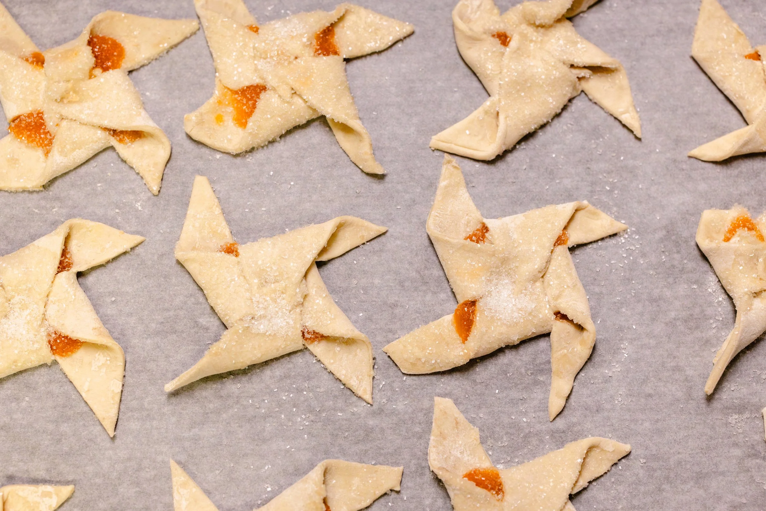 Unbaked star-shaped cookies with orange filling on a baking sheet lined with parchment paper, dusted with powdered sugar.