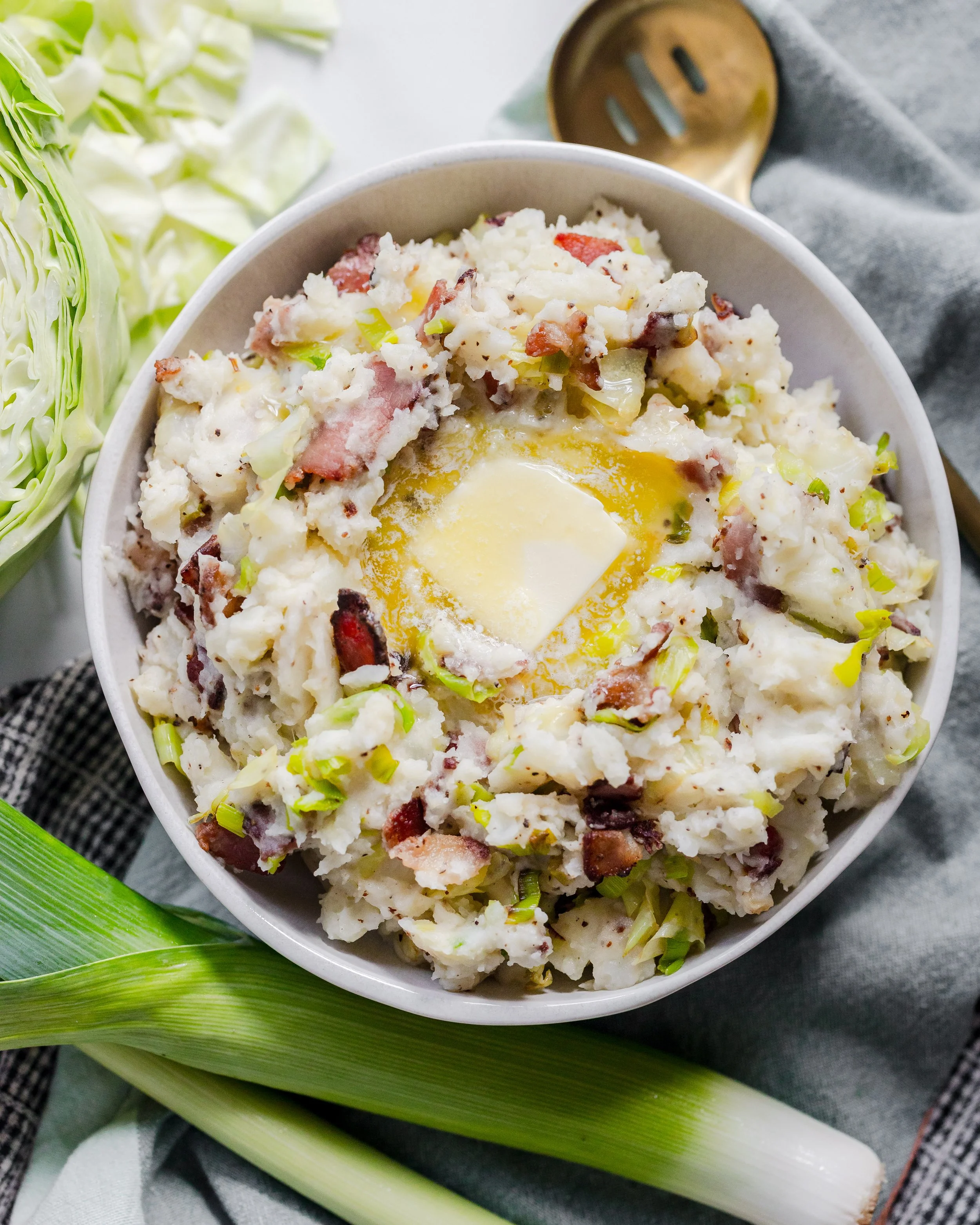 Bowl of potato salad with chopped bacon and sliced celery, topped with melting butter.