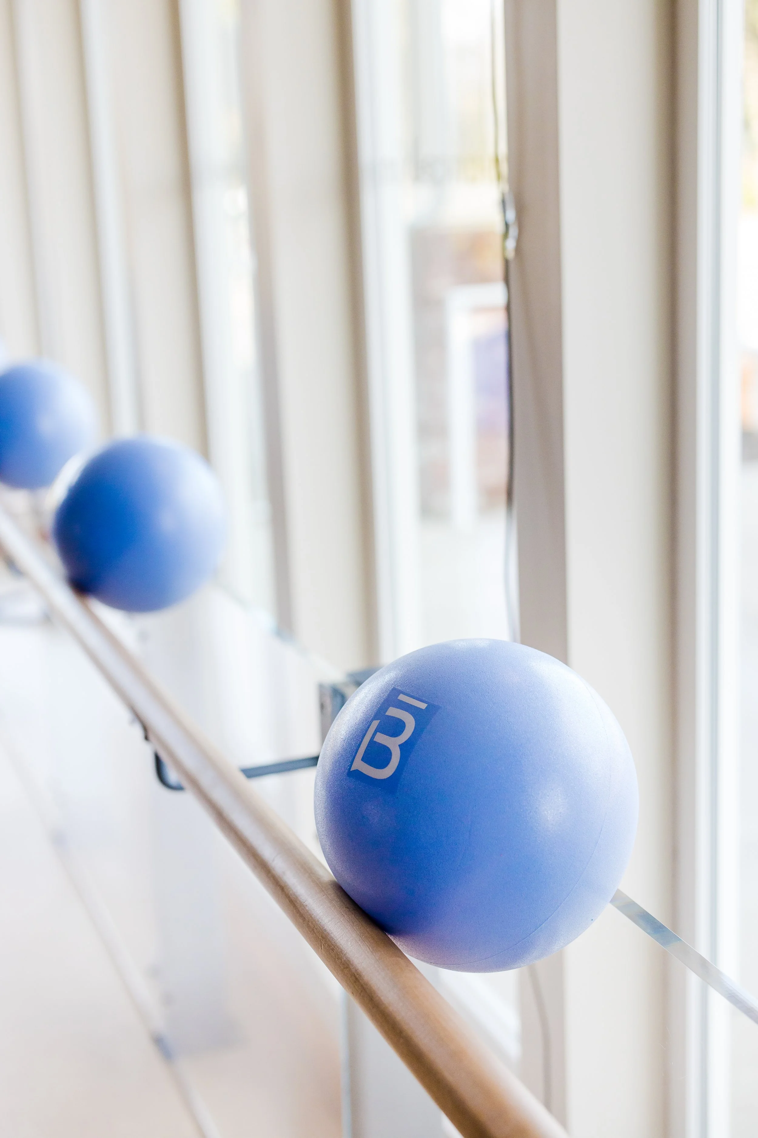 Blue exercise balls resting on a ballet barre near large windows.