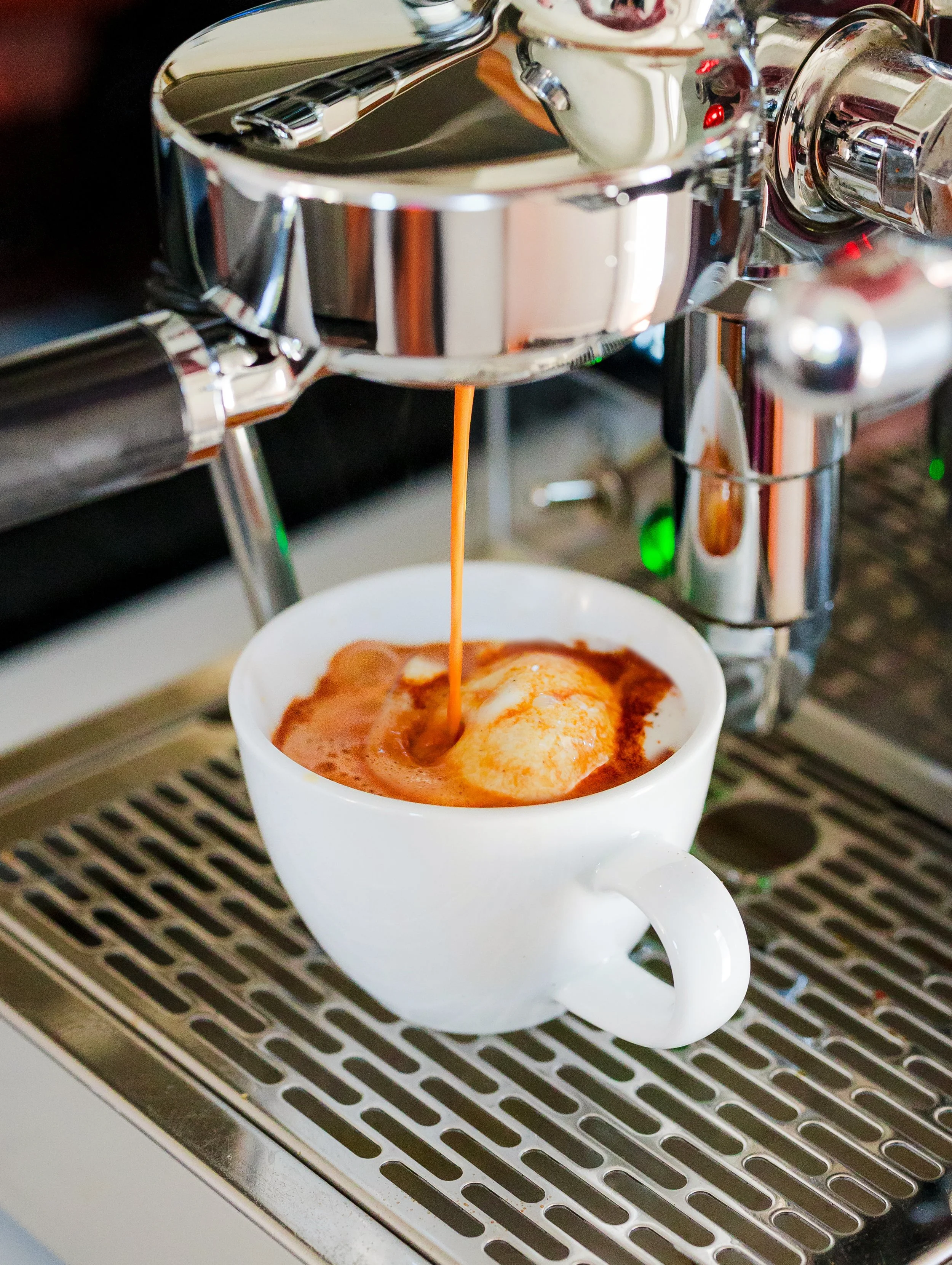 Close-up of espresso shot brewing into a white ceramic cup from a shiny Italian espresso machine.