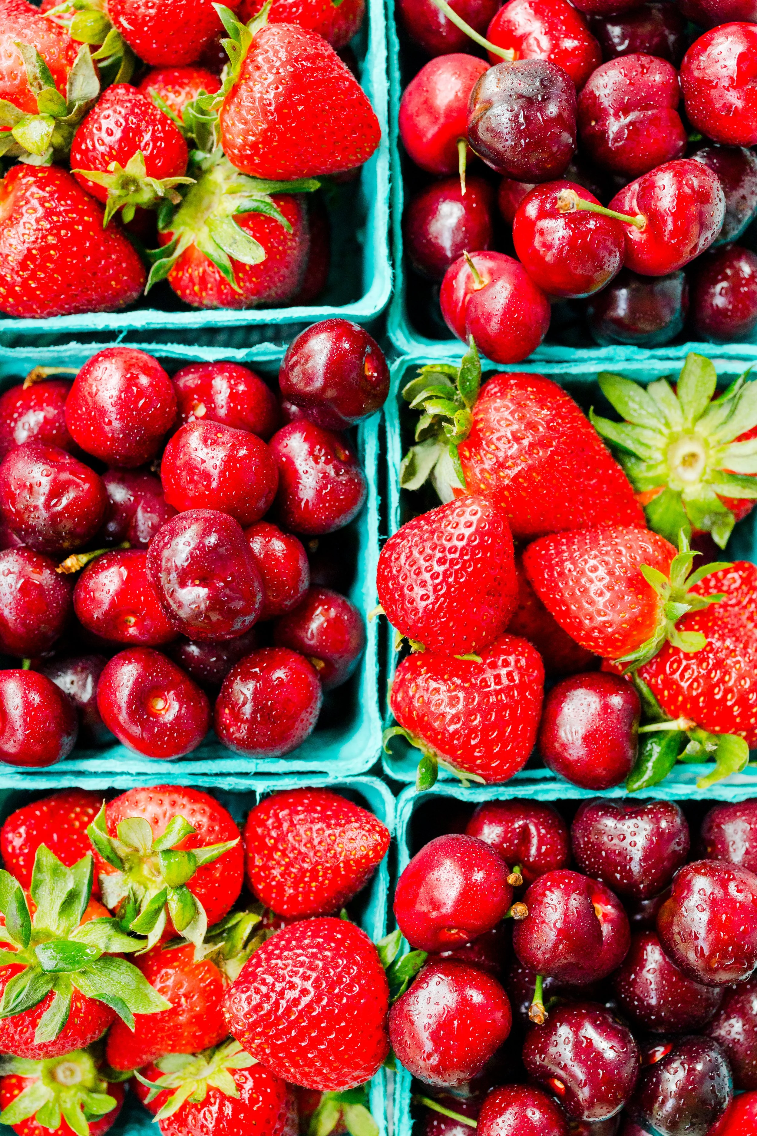 Fresh strawberries and cherries in blue containers at a market.