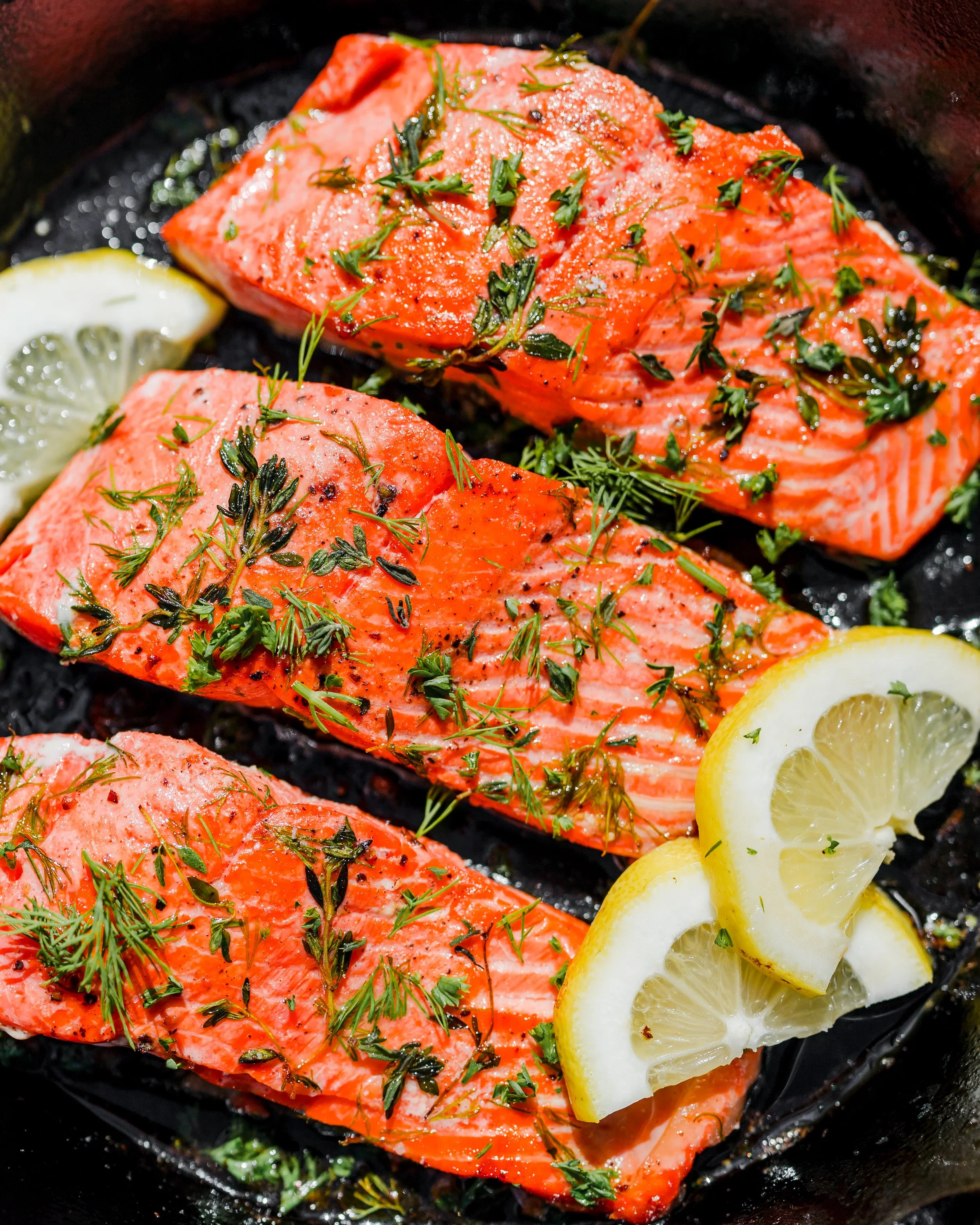 Cooked salmon fillets garnished with chopped herbs and lemon slices.