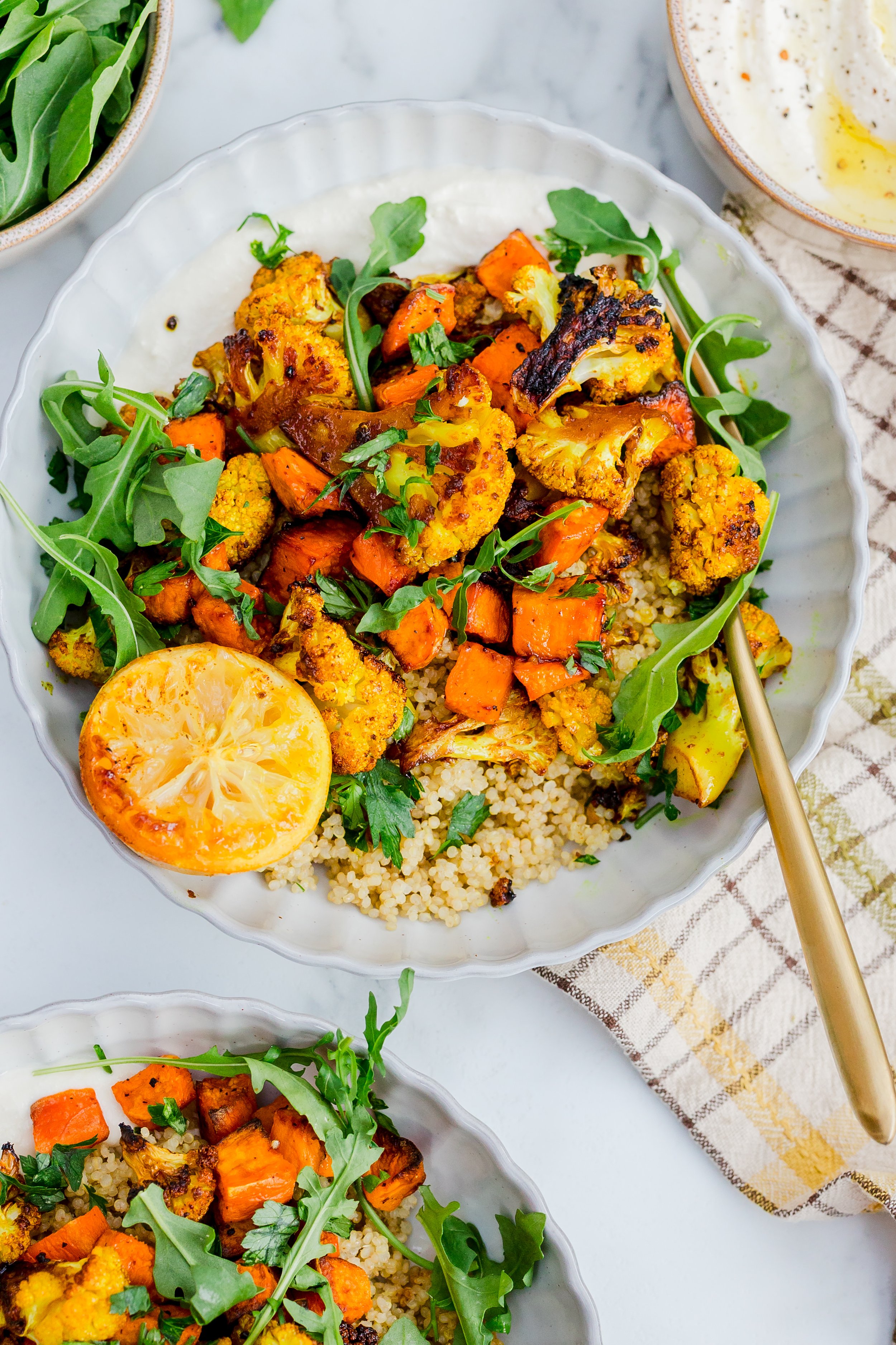 Roasted cauliflower and sweet potato salad with quinoa, garnished with fresh herbs and a grilled lemon half.