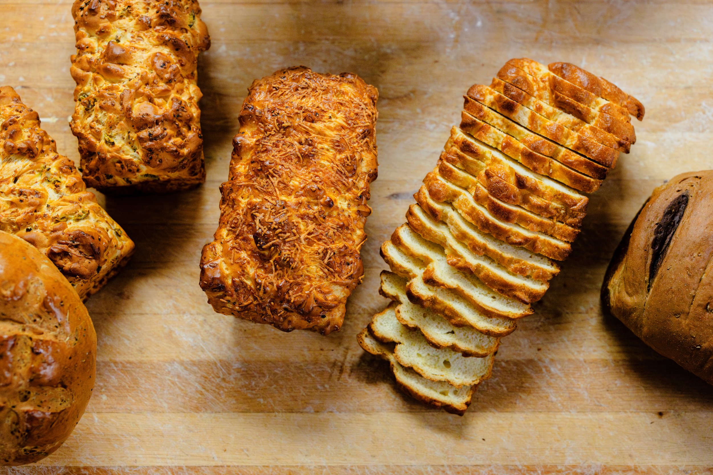 Various sliced and whole loaves of bread on a wooden cutting board.