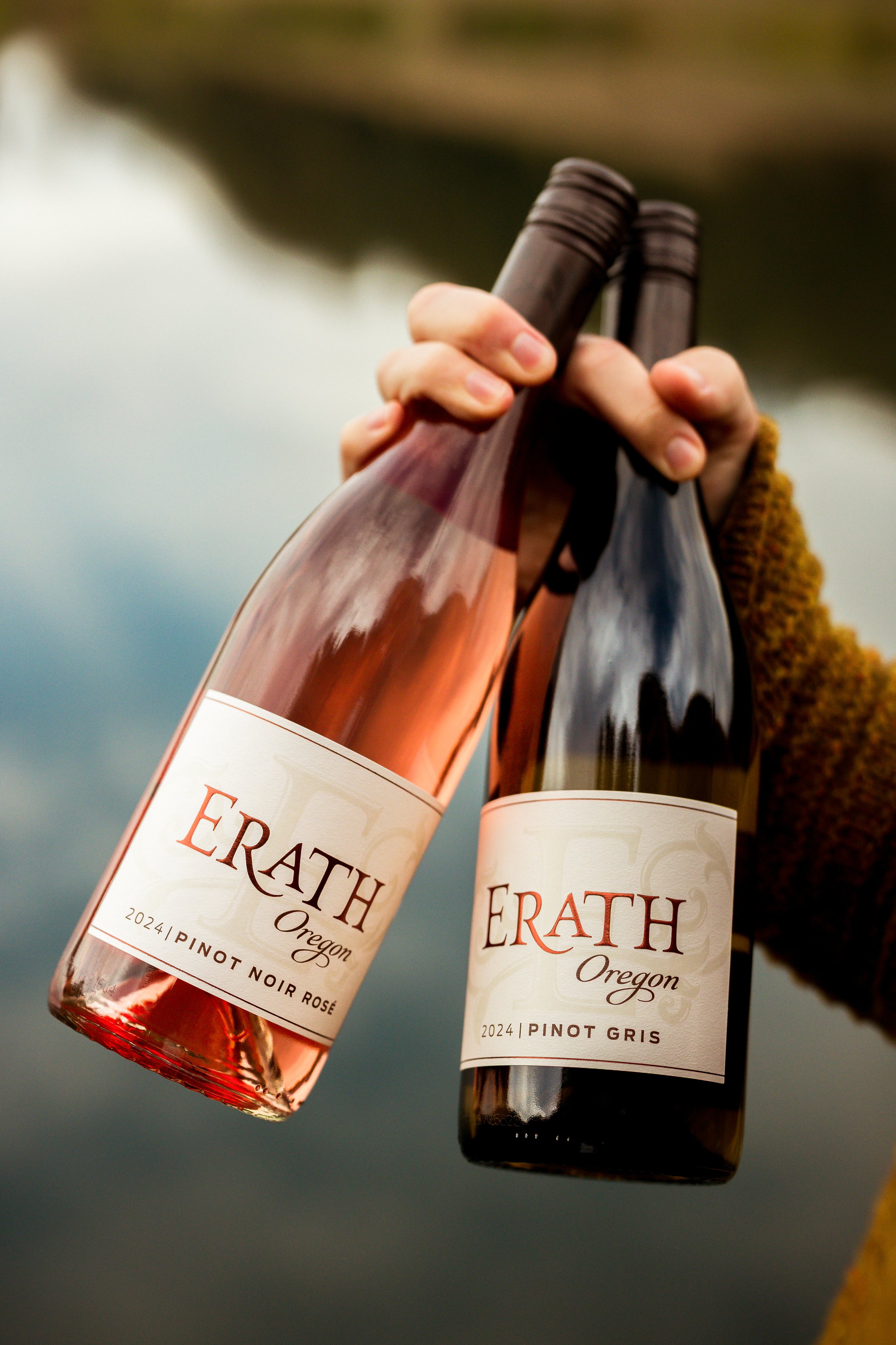 Two wine bottles labeled 'ERATH Oregon' being held outdoors with a blurred water and sky background.