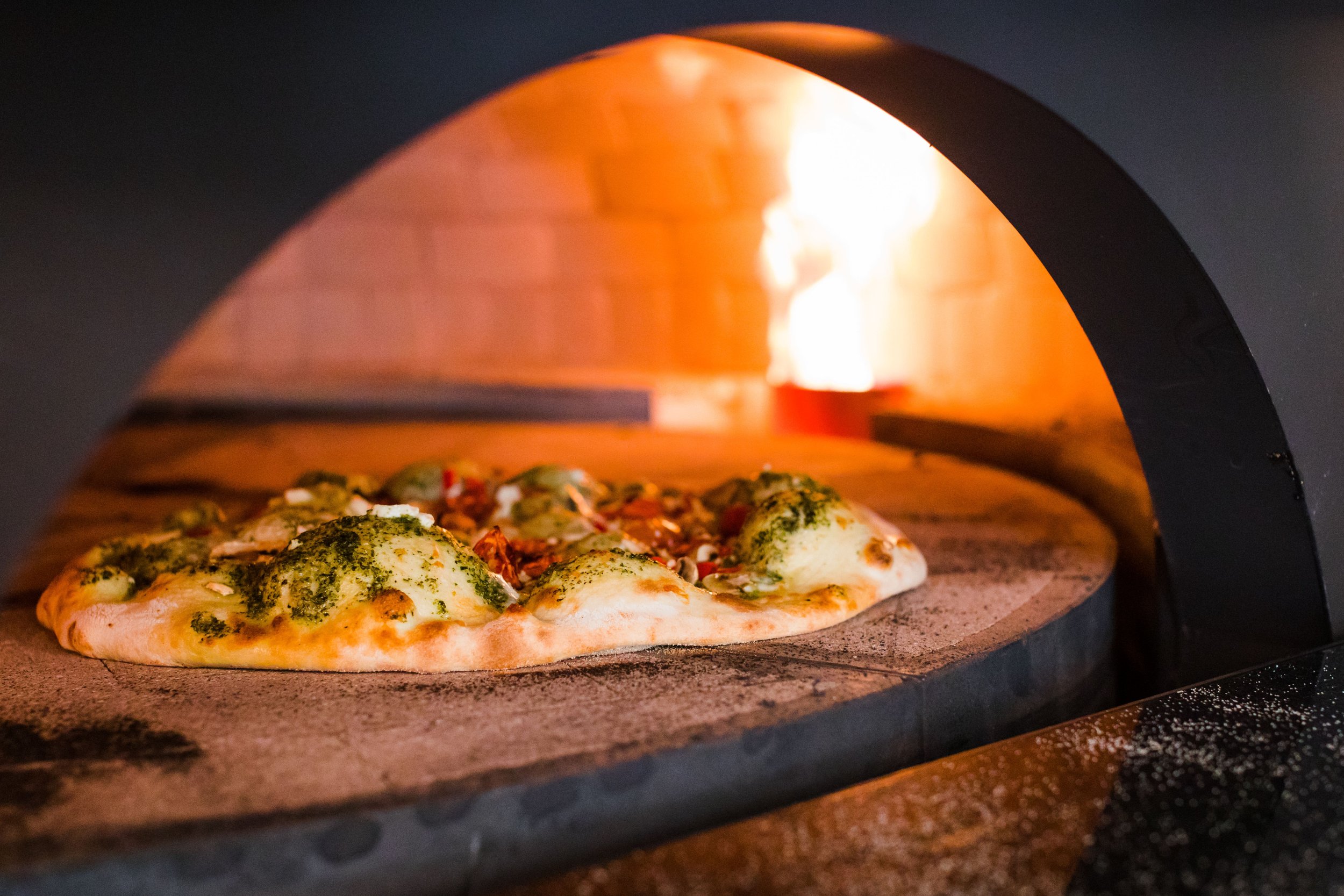 Pizza baking inside a home wood-fired oven with a glowing fire in the background.