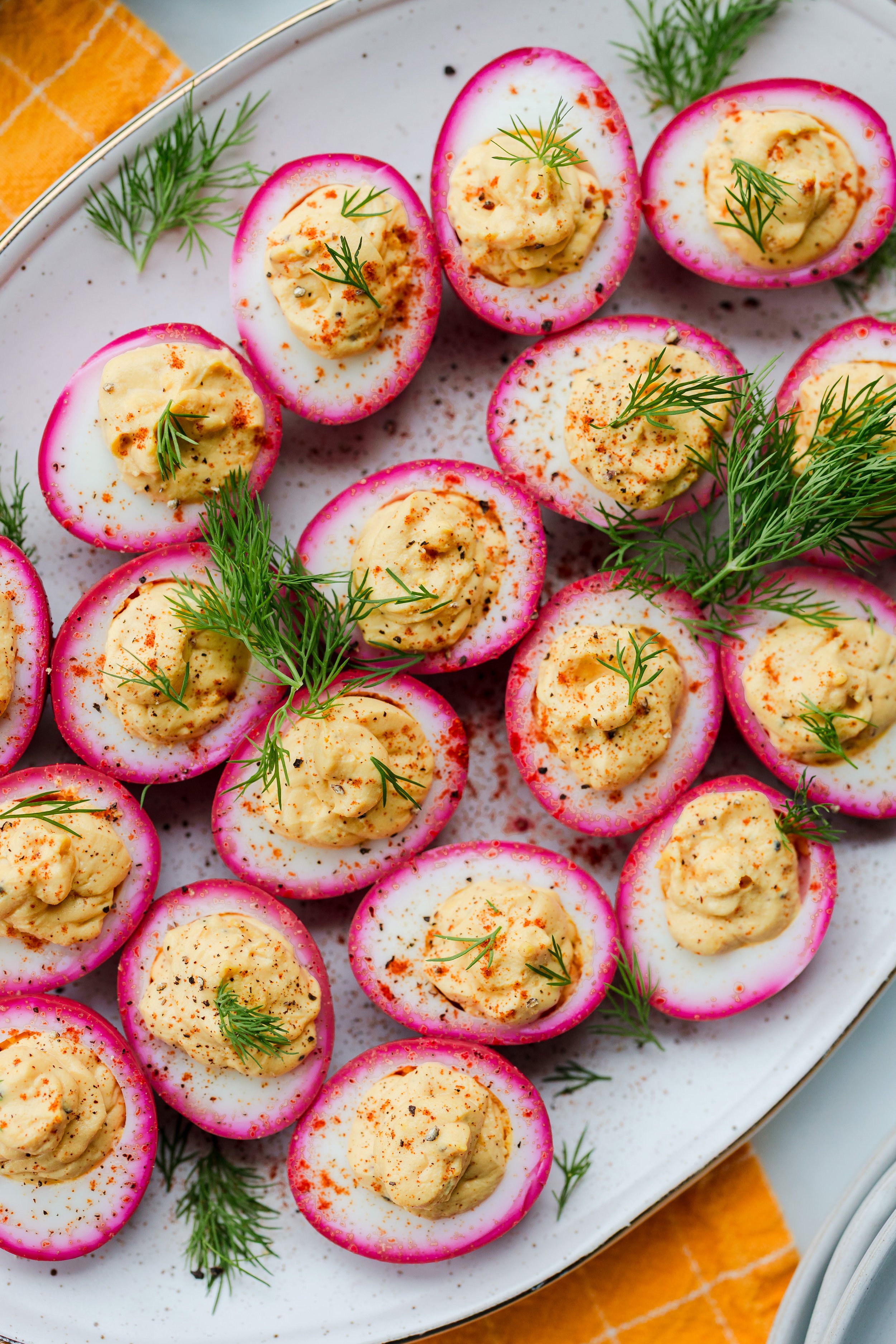 Halved soft-boiled eggs with pink edges topped with seasoned egg yolk mixture garnished with fresh dill on a white platter
