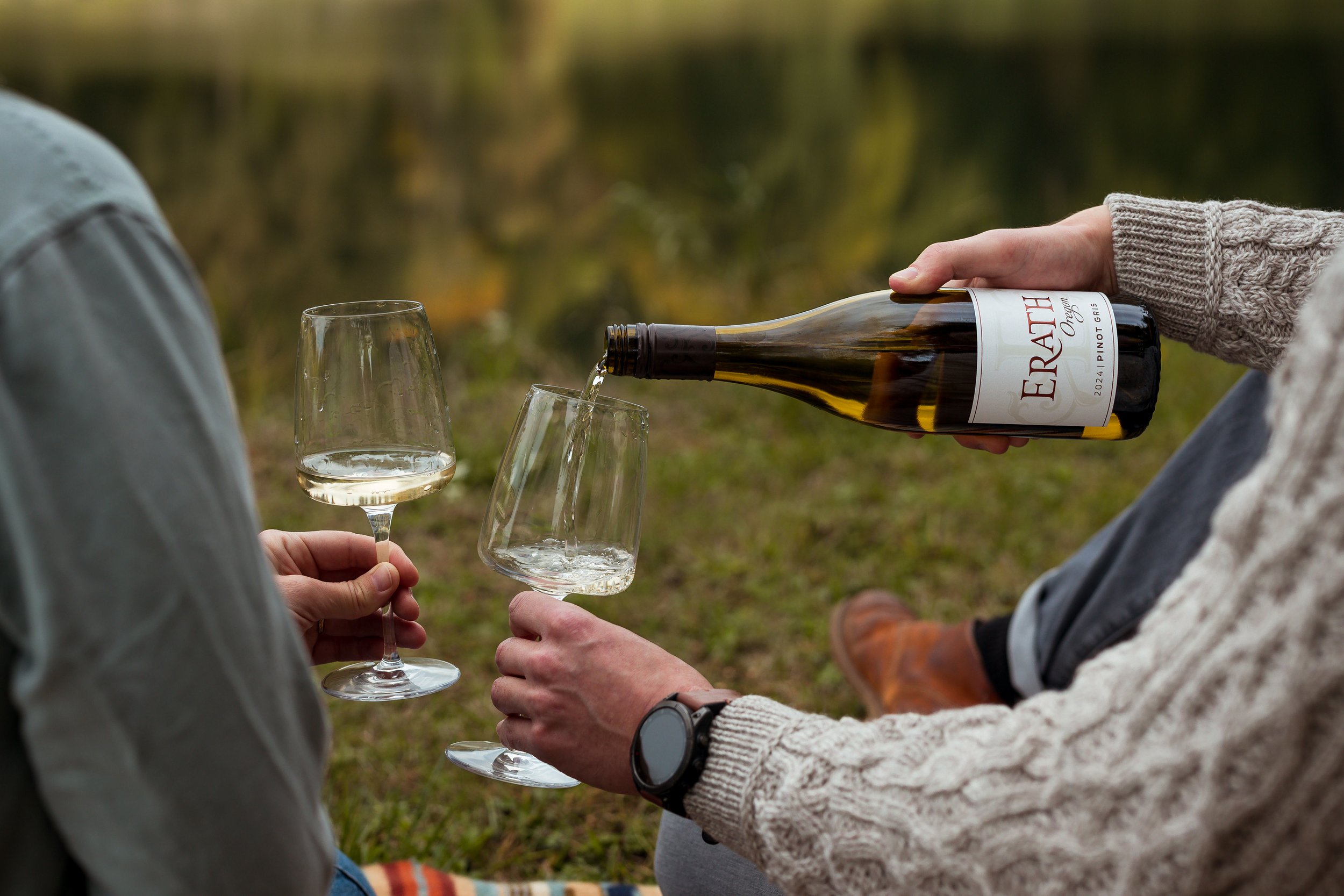 Person pouring wine into a glass outdoors during daytime.