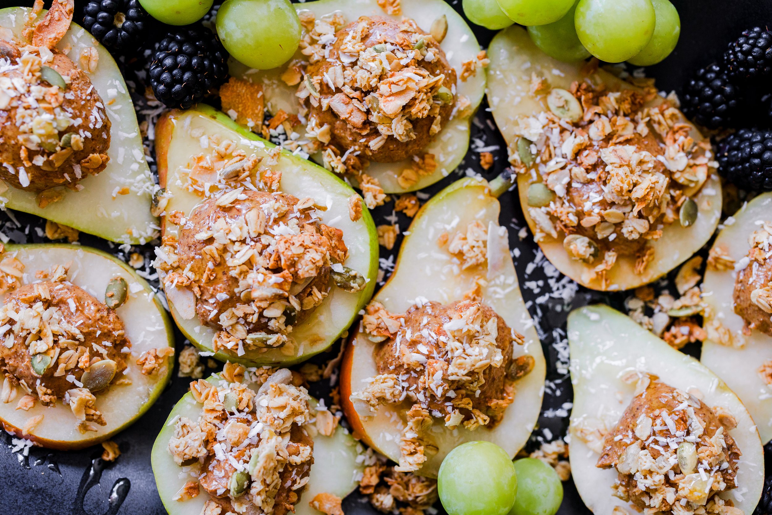 Green and red pear halves topped with granola, seeds, and shredded coconut, garnished with green grapes.