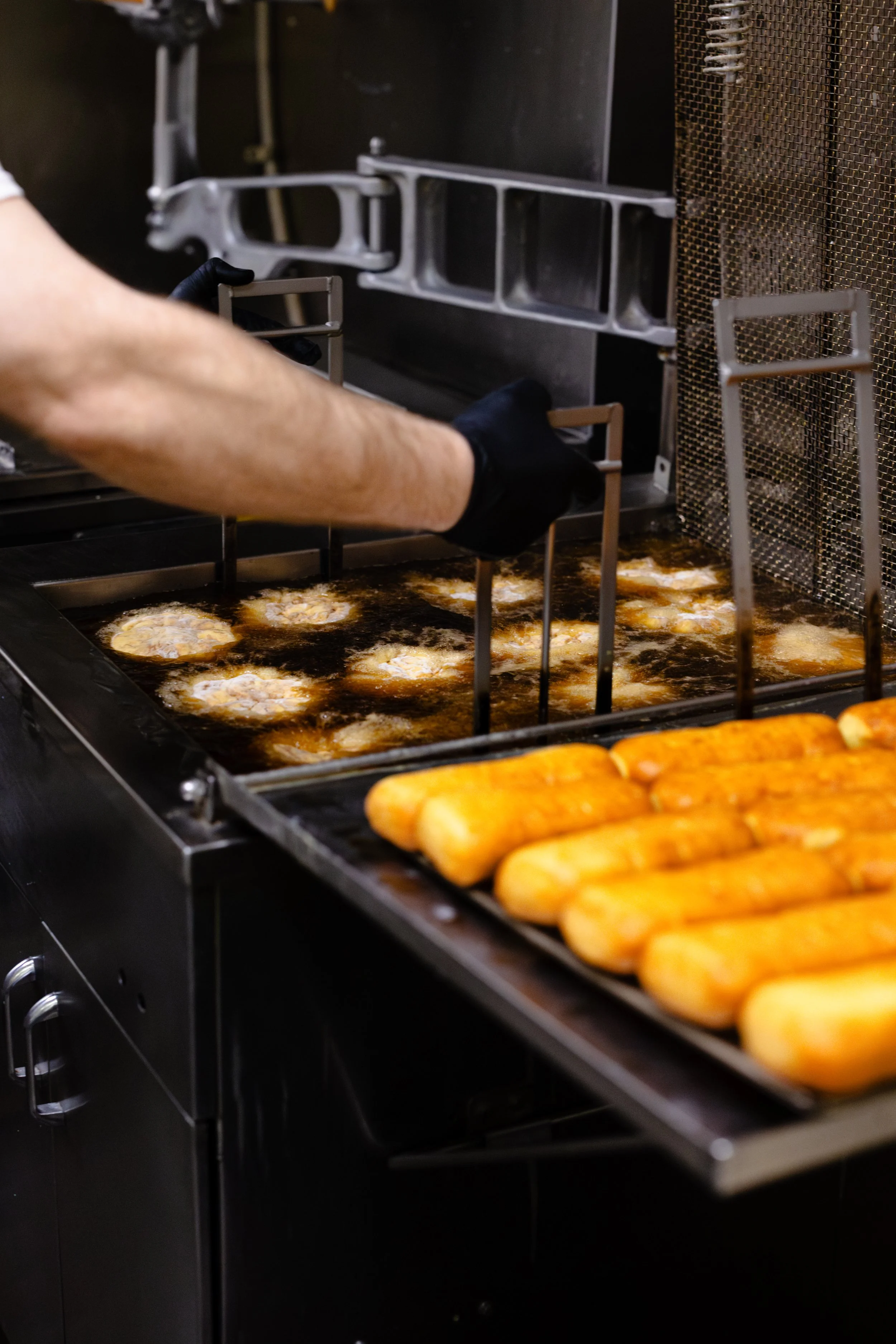 Someone frying chicken tenders in a commercial deep fryer with mozzarella sticks on a tray nearby.