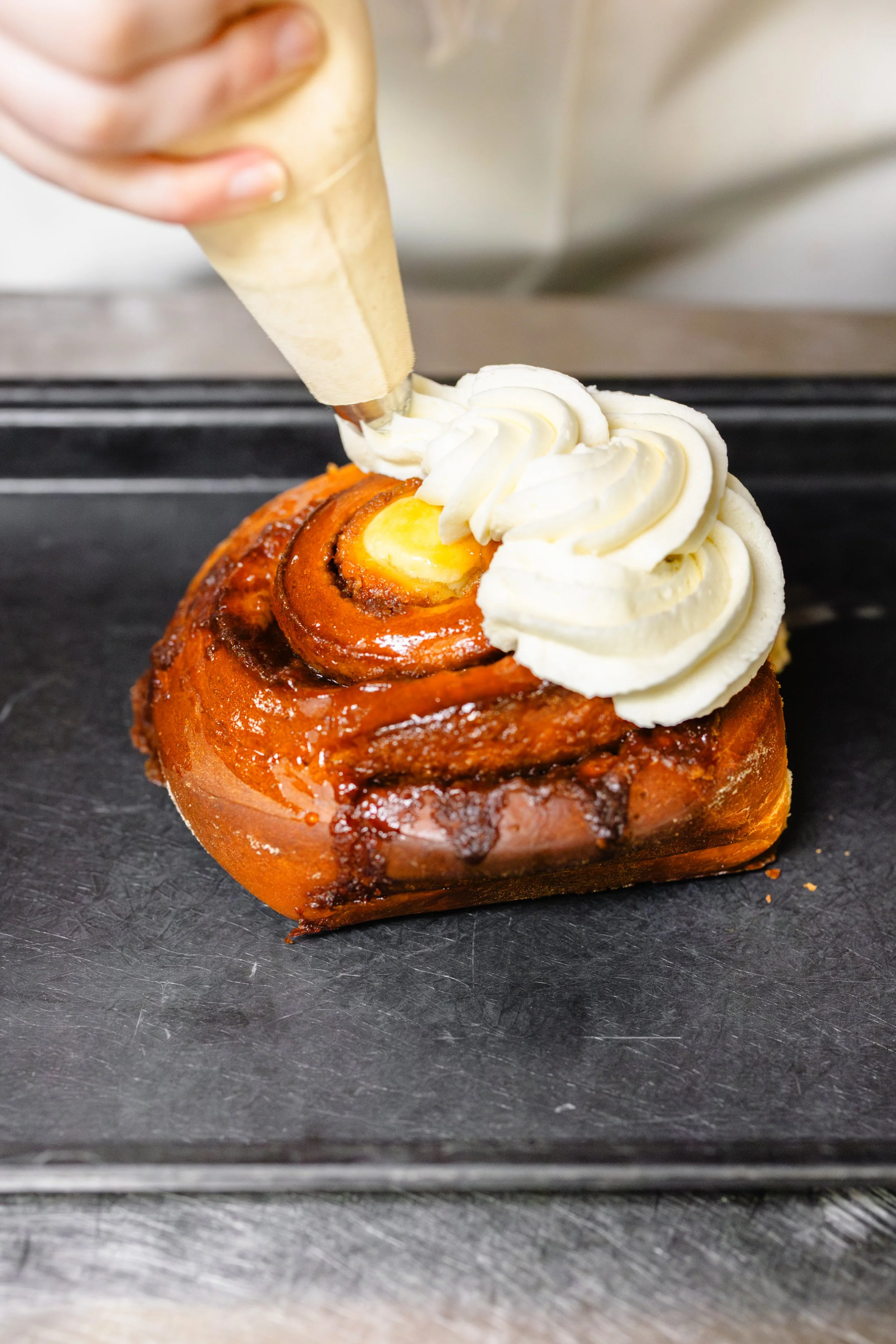 Decorating a cinnamon roll with white frosting using a piping bag.