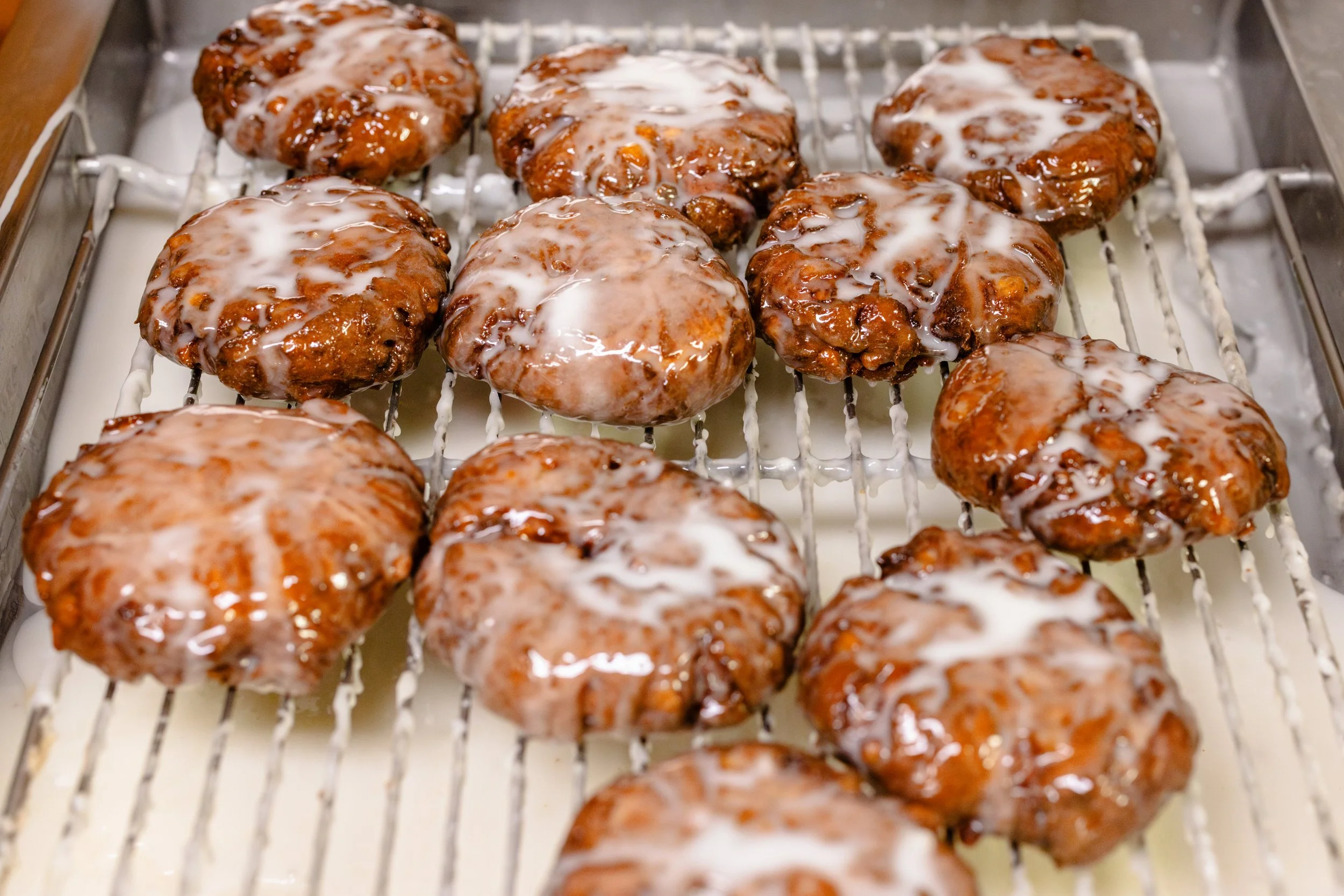 Nine glazed, cooked cinnamon rolls with icing on a metal cooling rack.