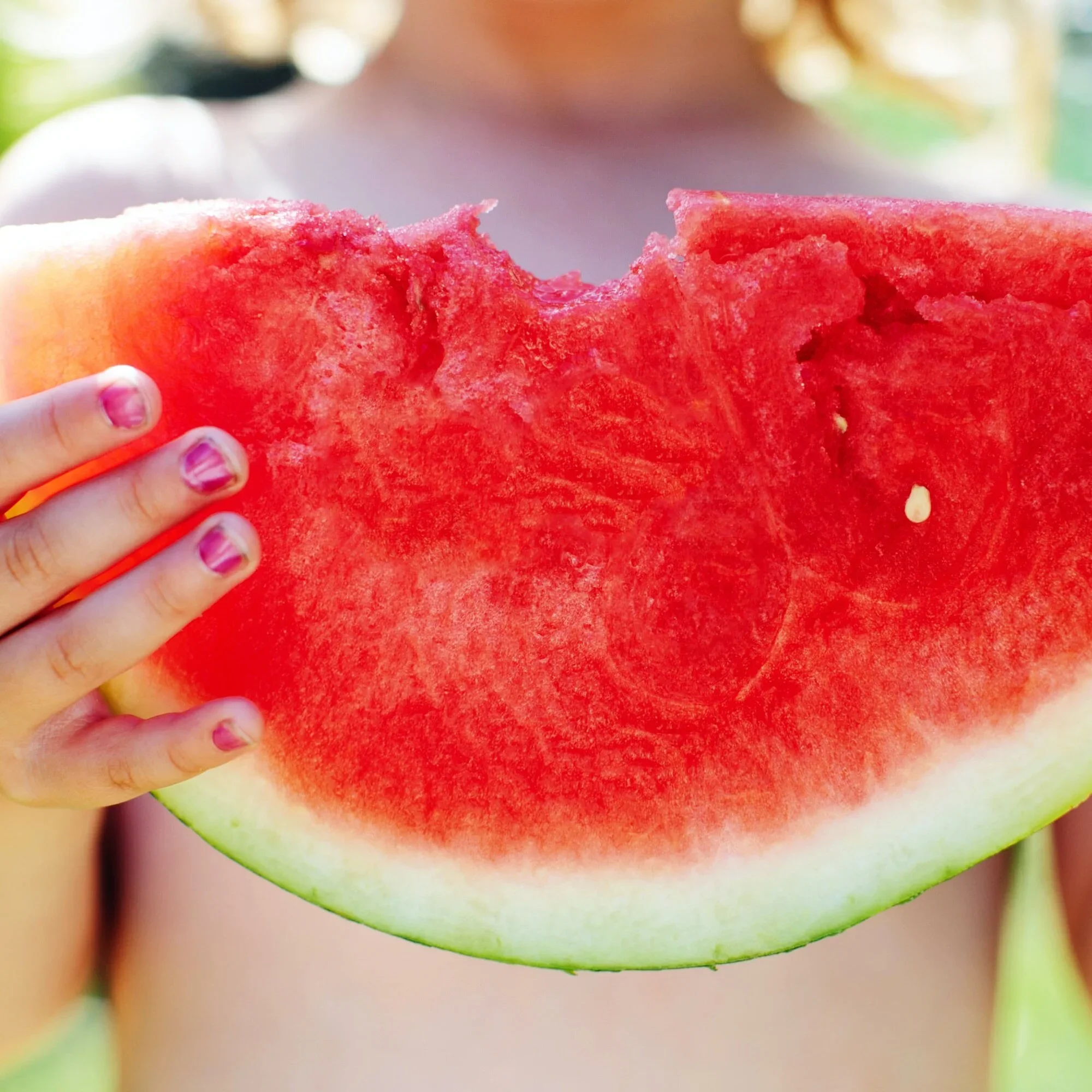 Child holding a large slice of watermelon outdoors.