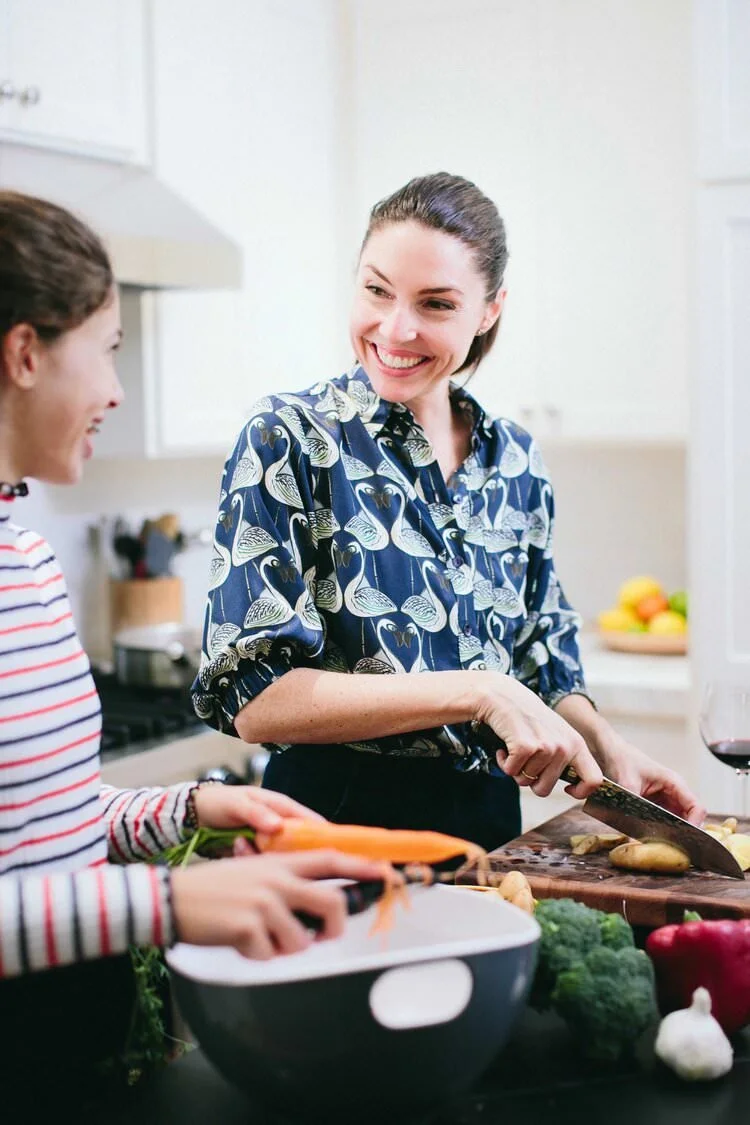Two women cooking together in a kitchen, smiling and chopping vegetables.