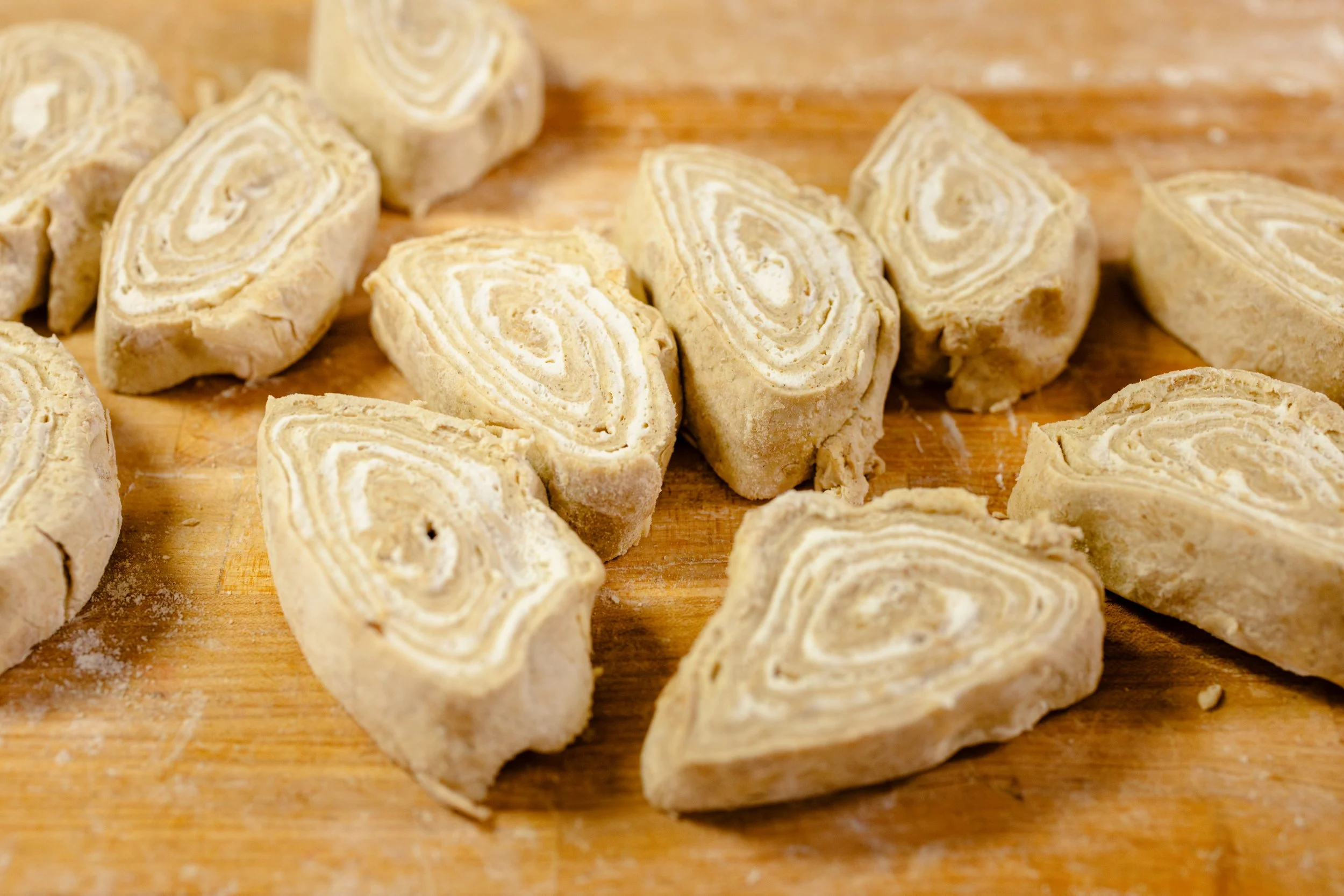 Sliced rolls of cinnamon bread with a spiral pattern on a wooden cutting board.