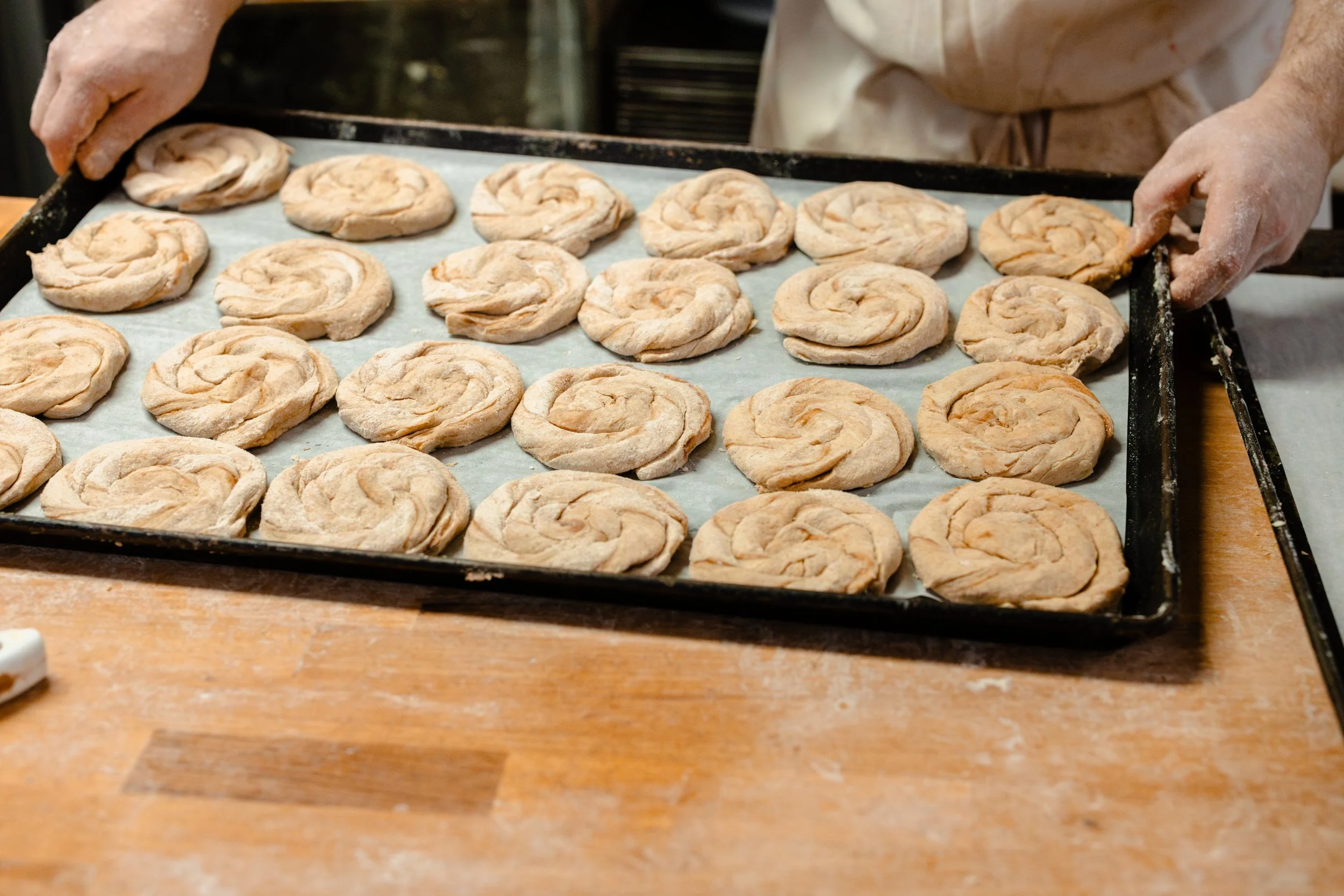 Baker holding a baking sheet with unbaked cinnamon rolls arranged in rows.
