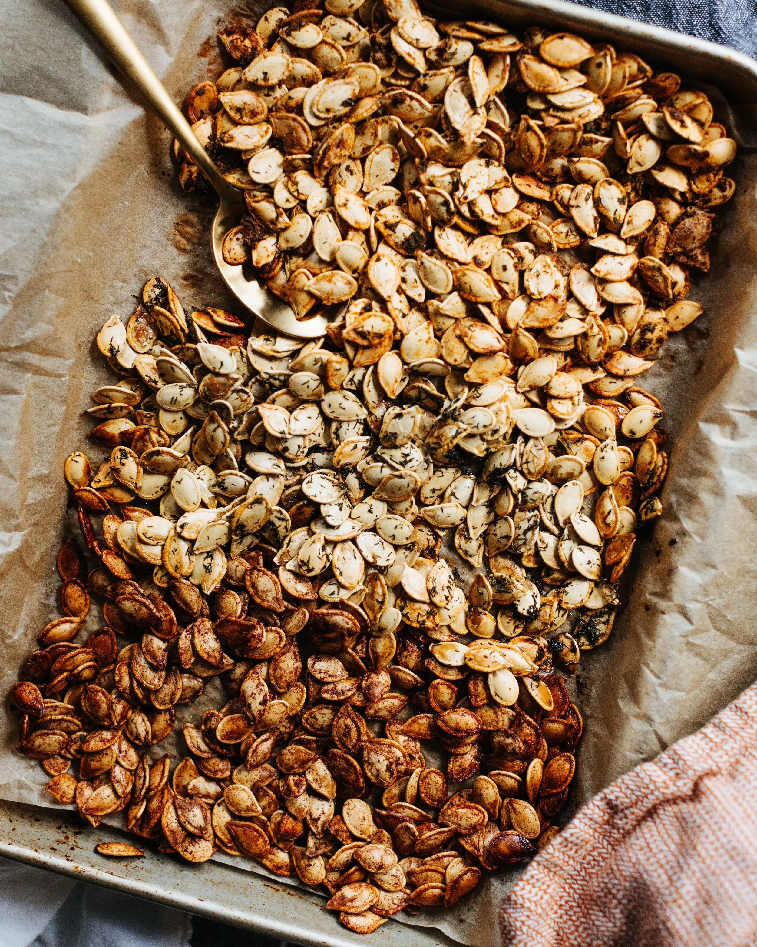 Roasted Sacha Inchi seeds on a baking sheet lined with parchment paper, with a metal scoop resting on top, and a textured cloth at the corner.
