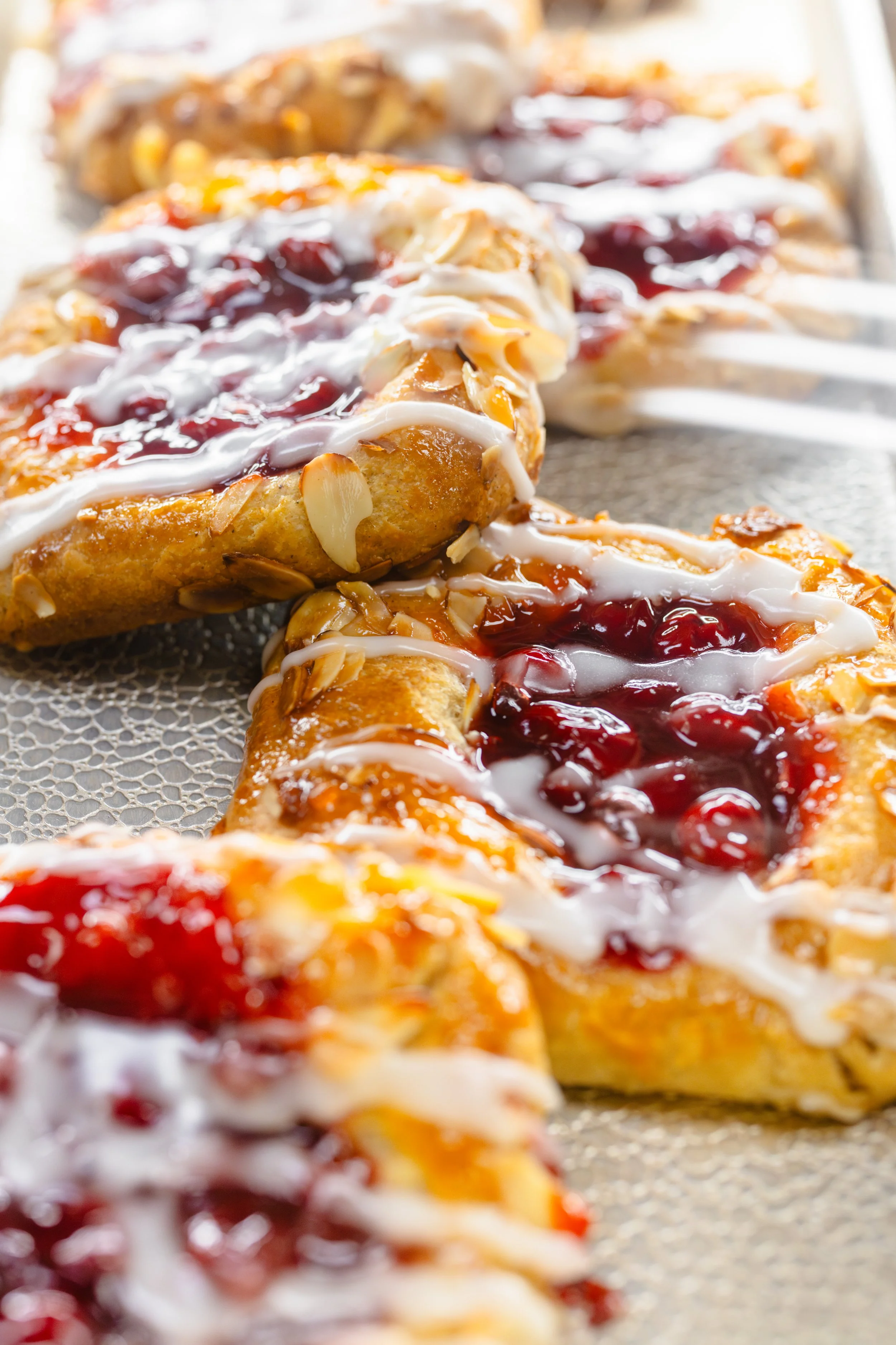 A close-up of baked pastry pizza with cherry topping, white icing, and sliced almonds.