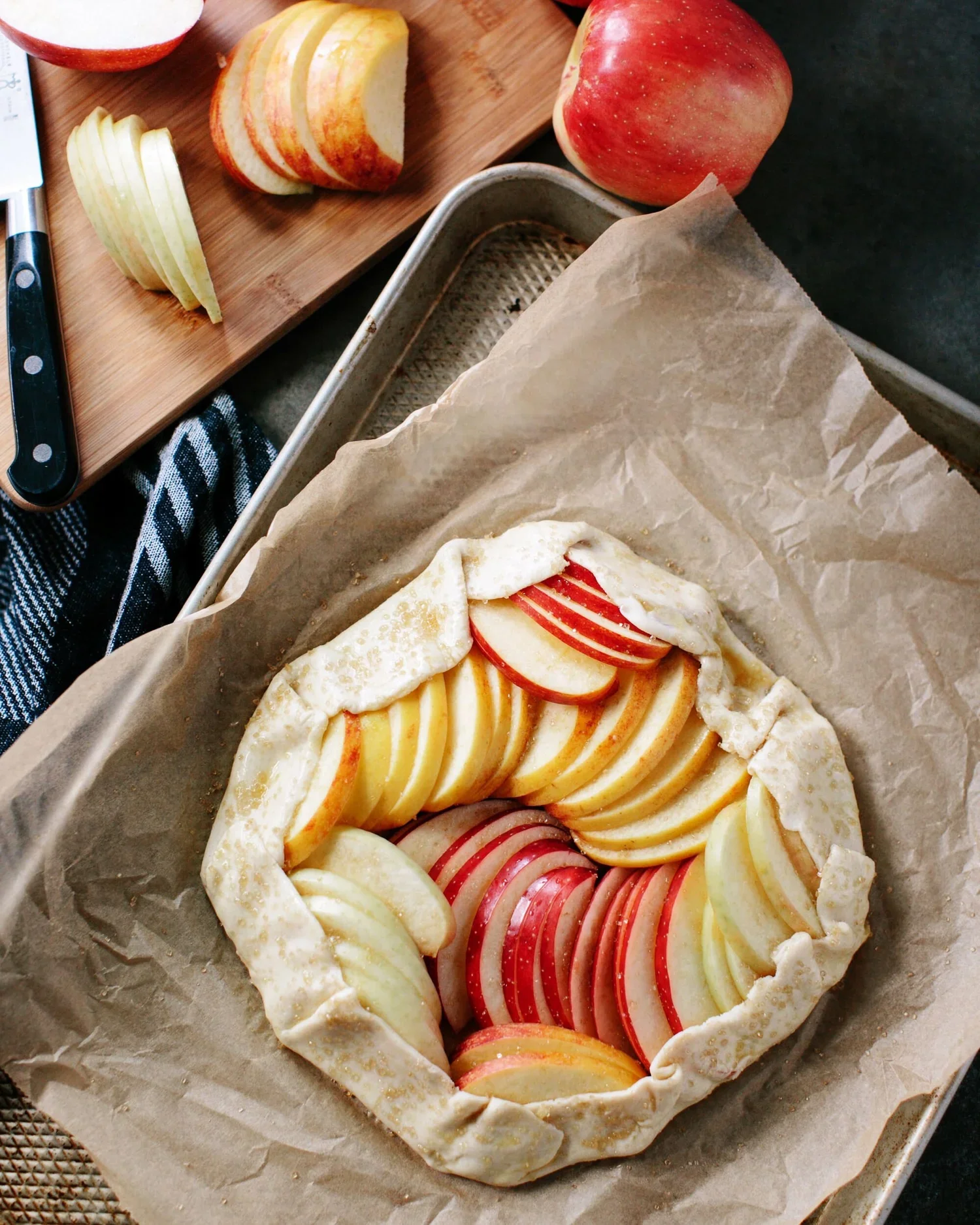 Unbaked apple galette with sliced apples inside a rustic pastry crust on a baking sheet