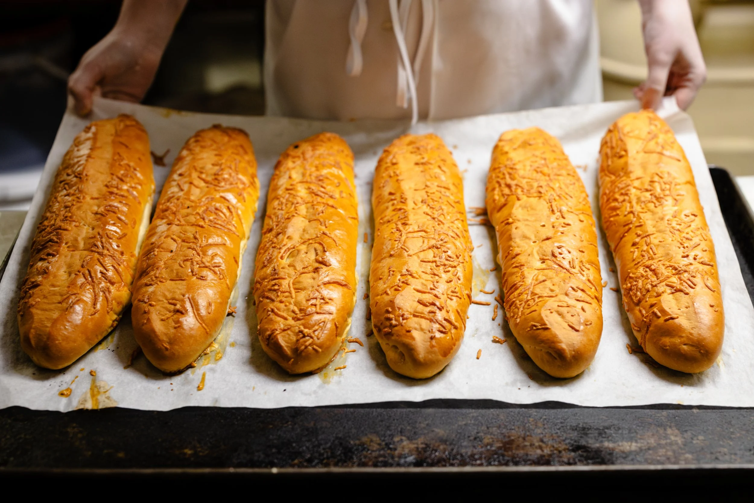 Six freshly baked bread rolls topped with melted cheese on a baking sheet.
