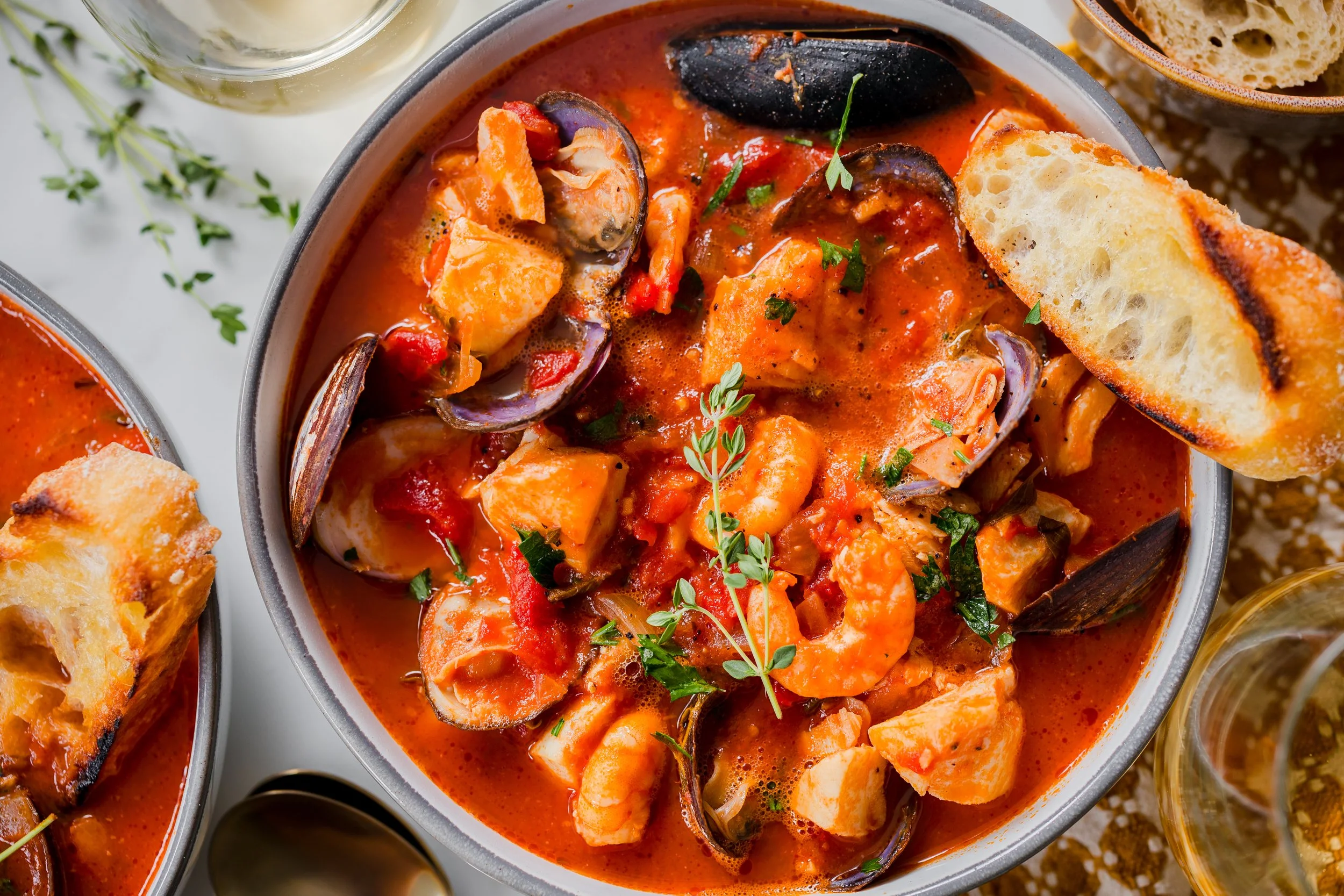 Seafood cioppino with shrimp, mussels, and chunks of fish in a tomato broth, garnished with herbs, served with toasted bread.