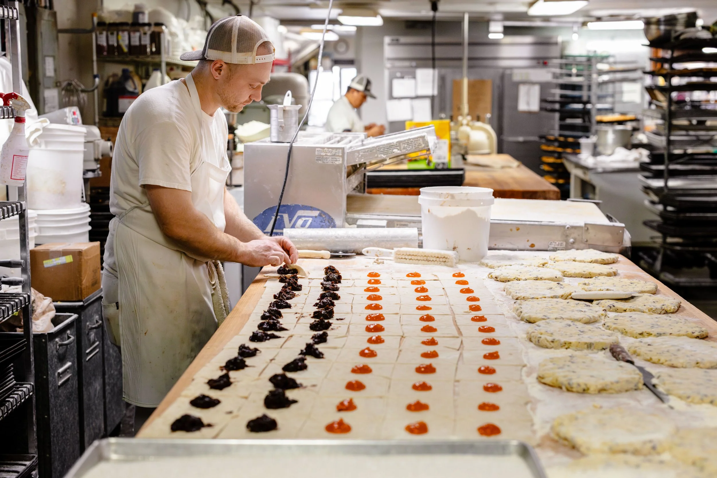 A chef preparing multiple sheets of food with black and orange fillings or toppings in a professional kitchen.
