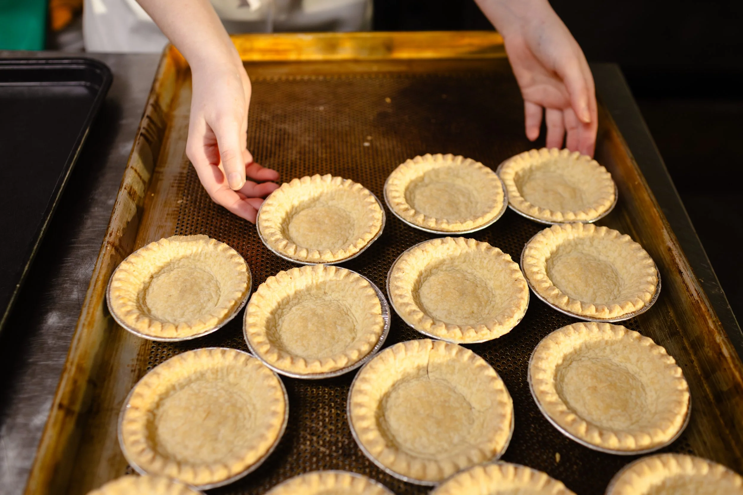 Hands placing small pie crusts into a baking tray for baking.